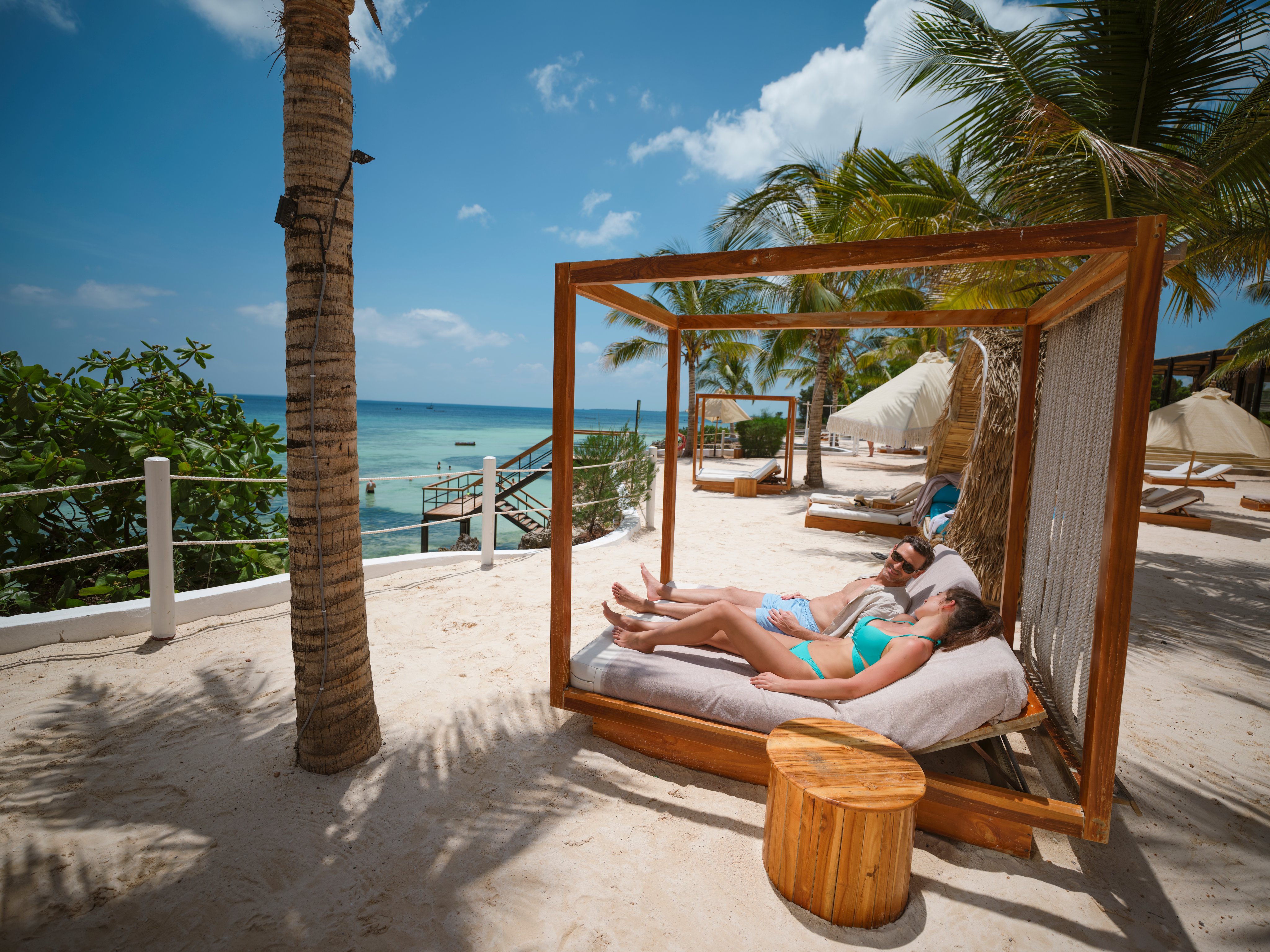 Entspannter Aufenthalt an einem Strand mit Liege im Schatten der Palmen am Meer.
