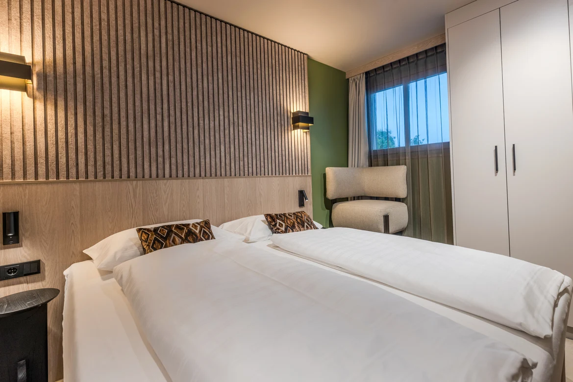 Modern Hotelzimmer von Aldiana mit Doppelbett, Sitzgelegenheit und Fenster mit Sicht in die Natur