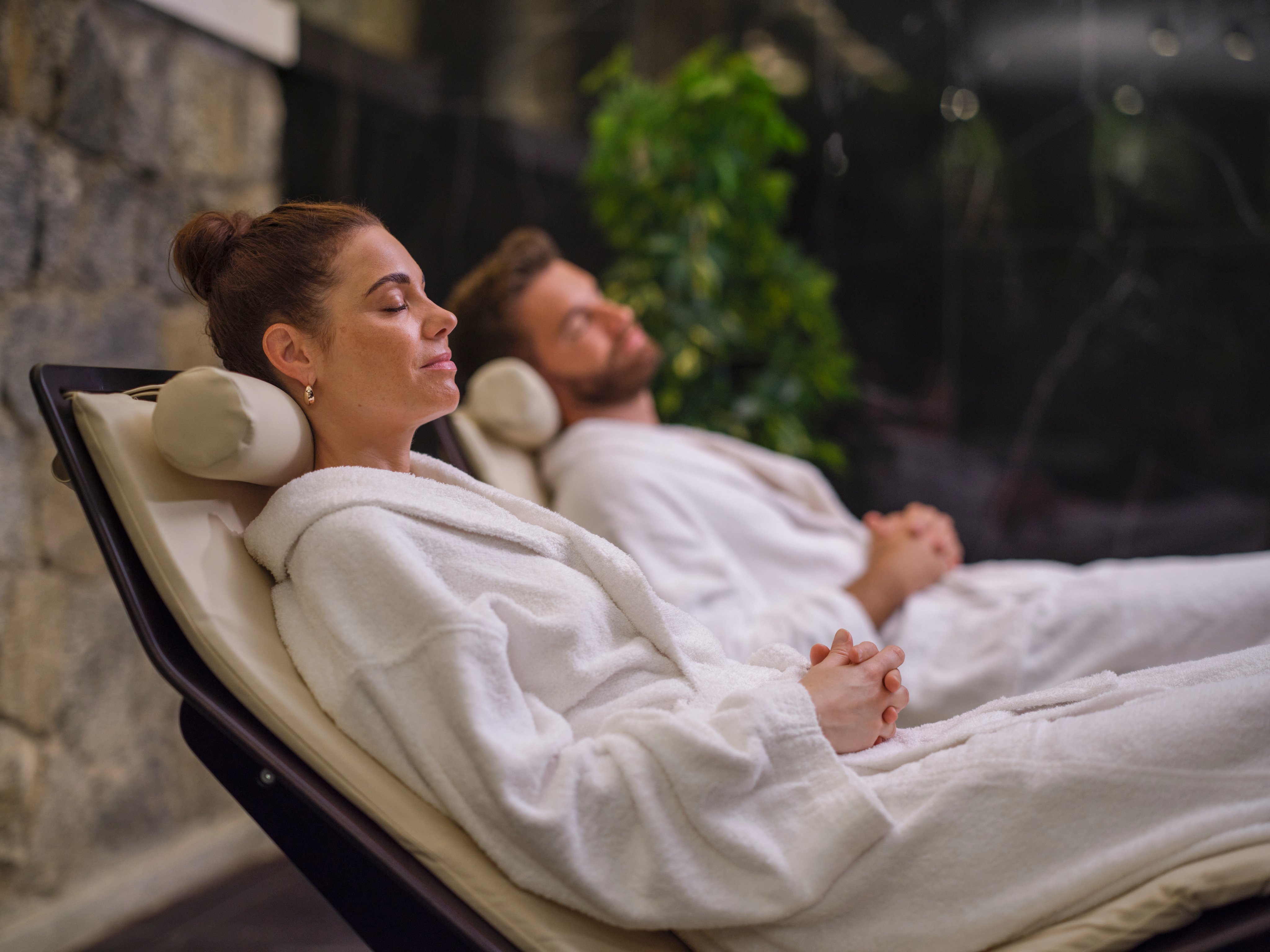 Zwei Personen entspannen im Wellnessbereich auf bequemen Liegen, umgeben von Natur und Ruhe