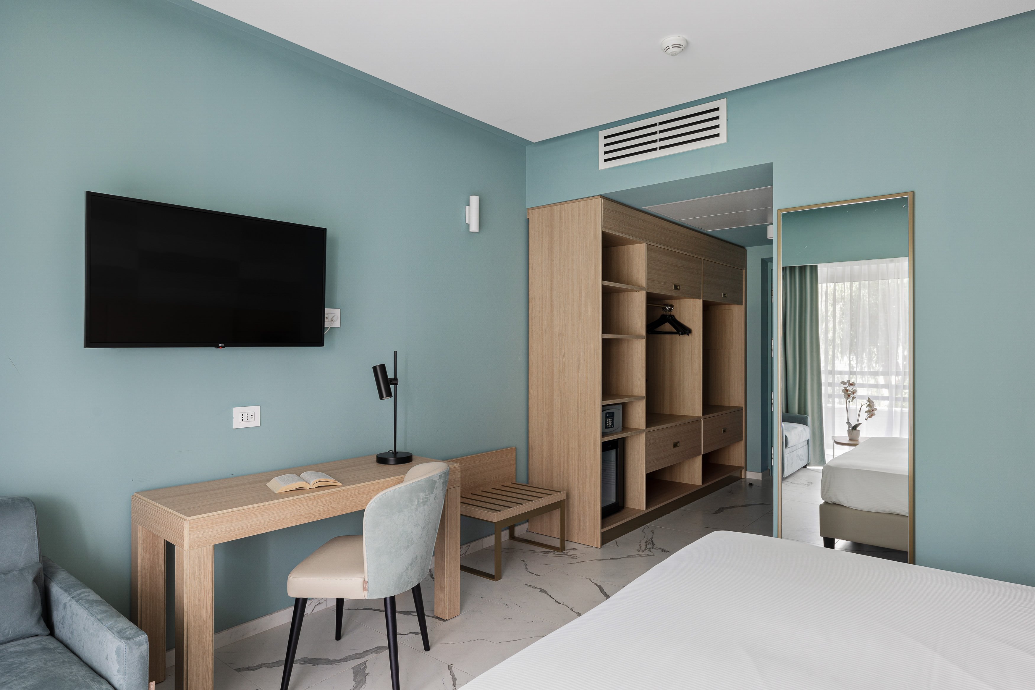 Geräumiges Hotelzimmer mit Fernseher, Schreibtisch, Kleiderschrank und Blick auf Balkon