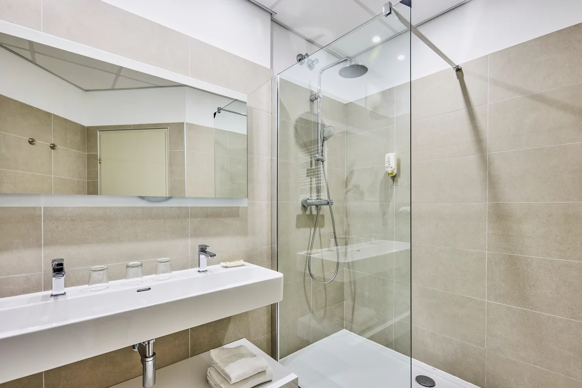 Ein modernes Badezimmer mit Dusche, großem Spiegel und Waschbecken im Premium Cluburlaub