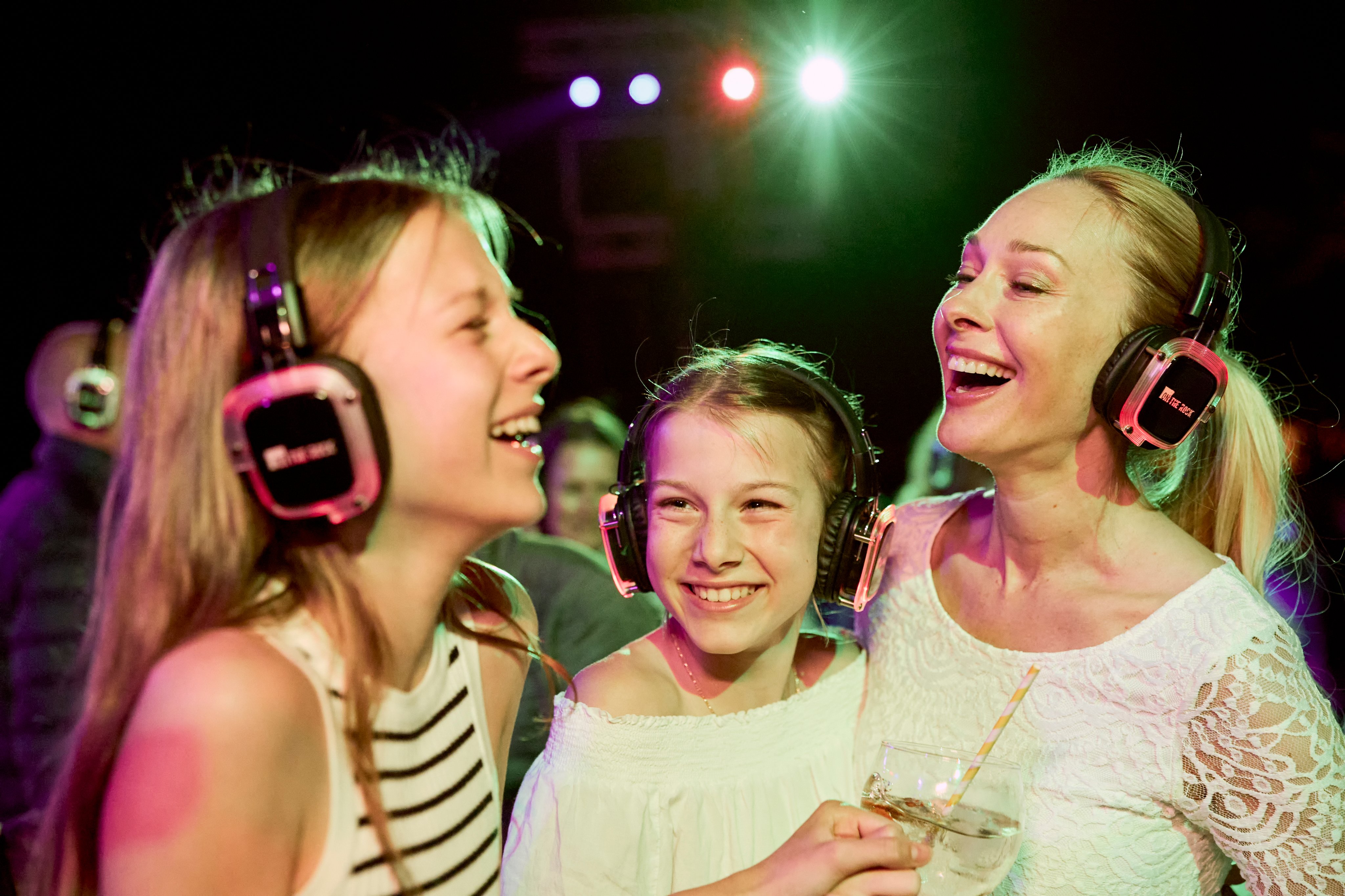 Drei Frauen mit Kopfhörern feiern bei einem Cluburlaub von Aldiana, fröhliche Atmosphäre.