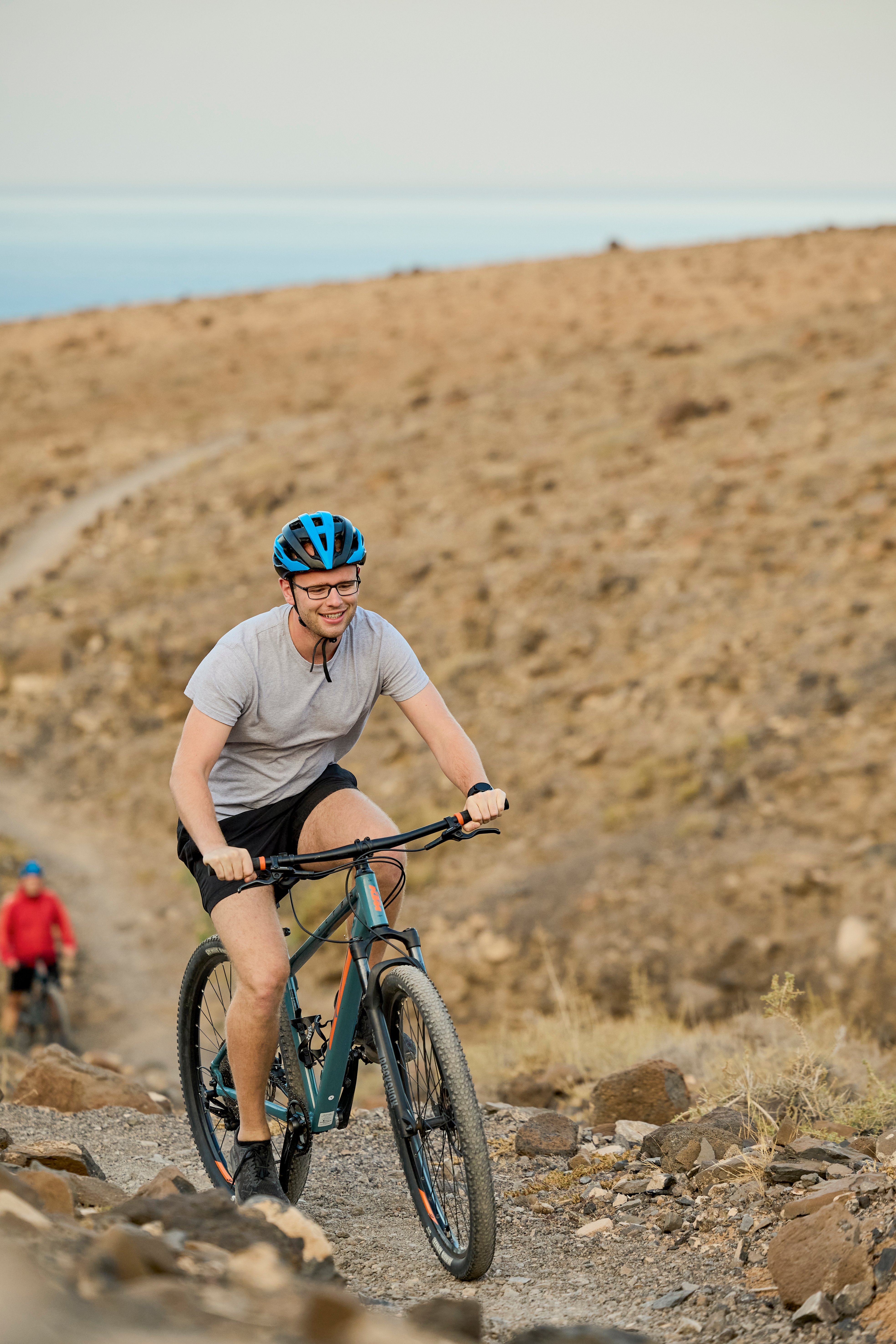 Frau fährt mit Fahrrad auf steiniger Naturstrecke im freien Gelände bei Sonnenschein