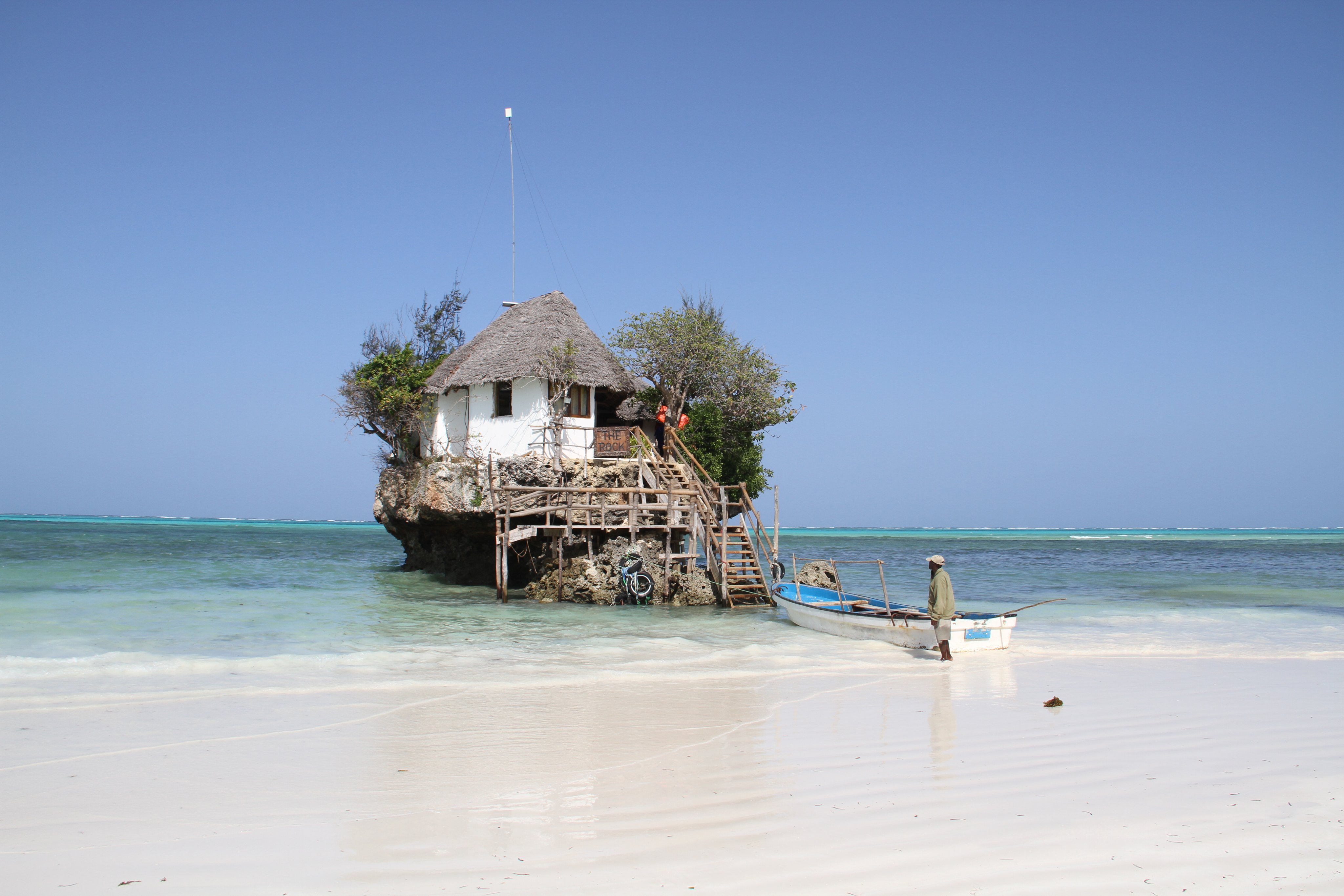 Ein idyllisches Haus auf einer kleinen Insel vor weißem Sandstrand und blauem Wasser
