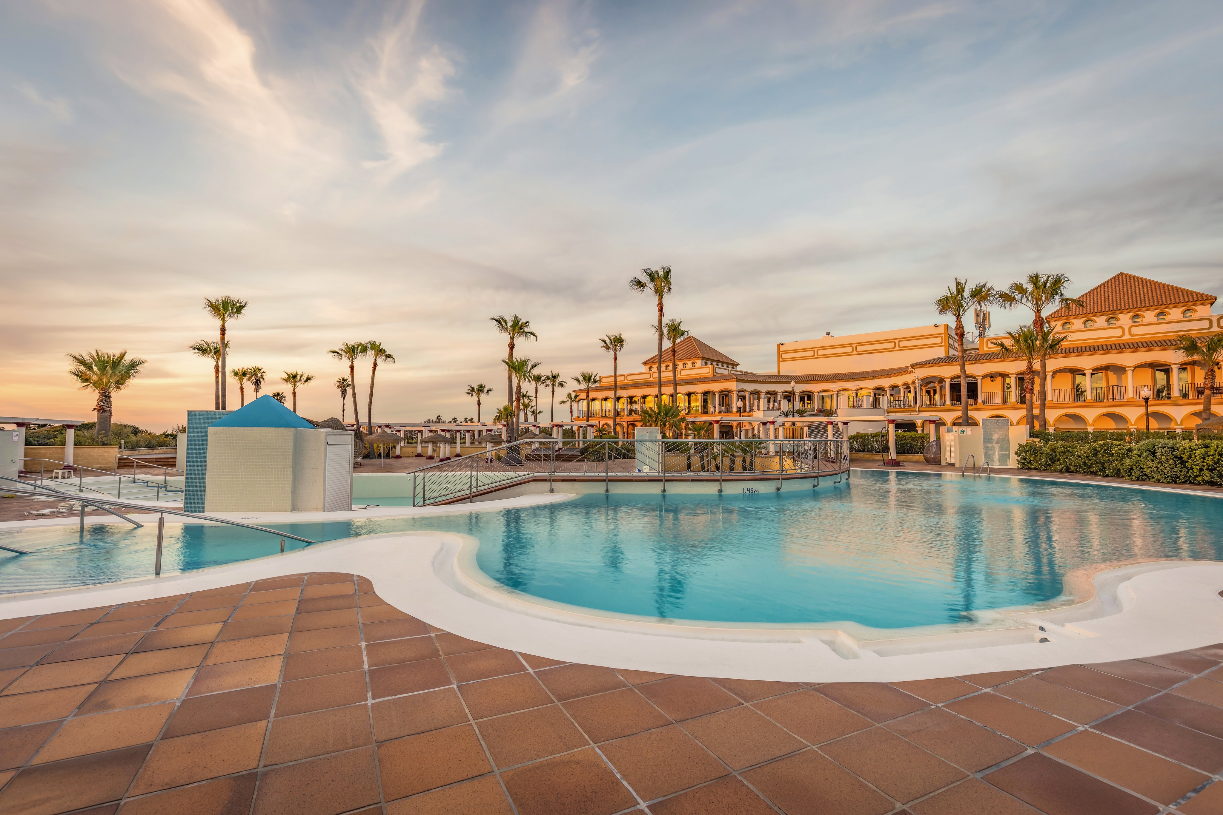 Luxuriöser Hotelpoolbereich bei Sonnenuntergang, Palmen, Premium Cluburlaub bei Aldiana