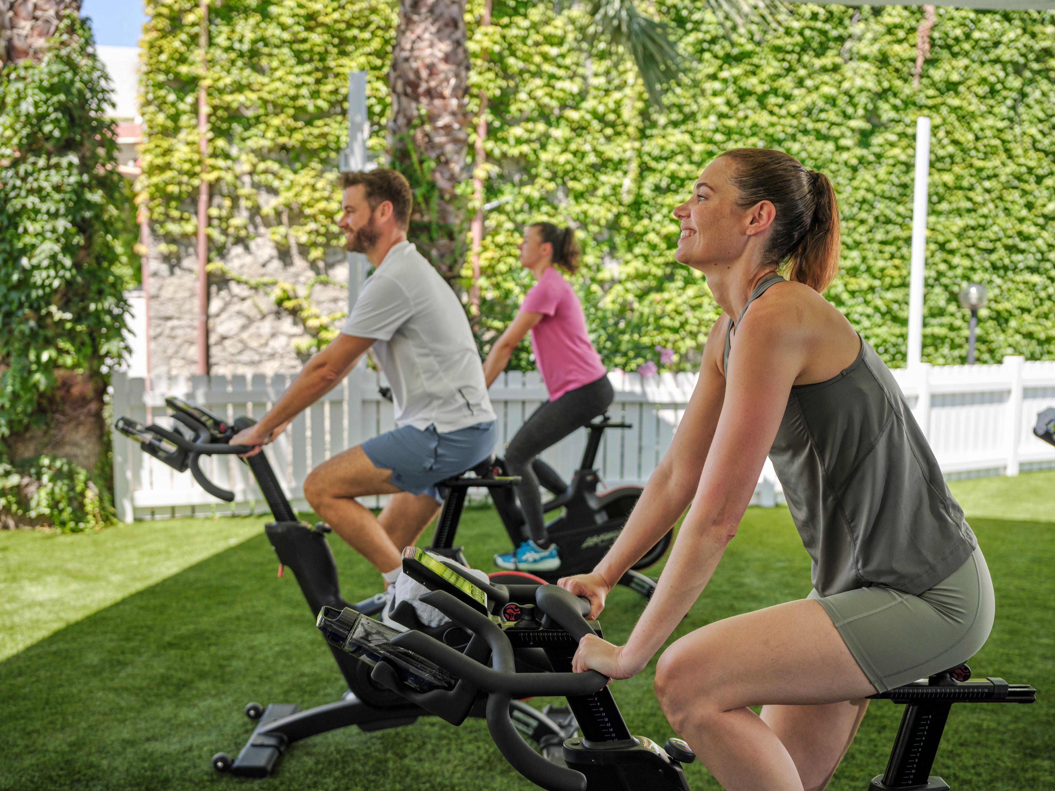 Menschen beim Training auf einem Rasen im Garten, eine Frau auf einem Indoor Cycling-Ergometer