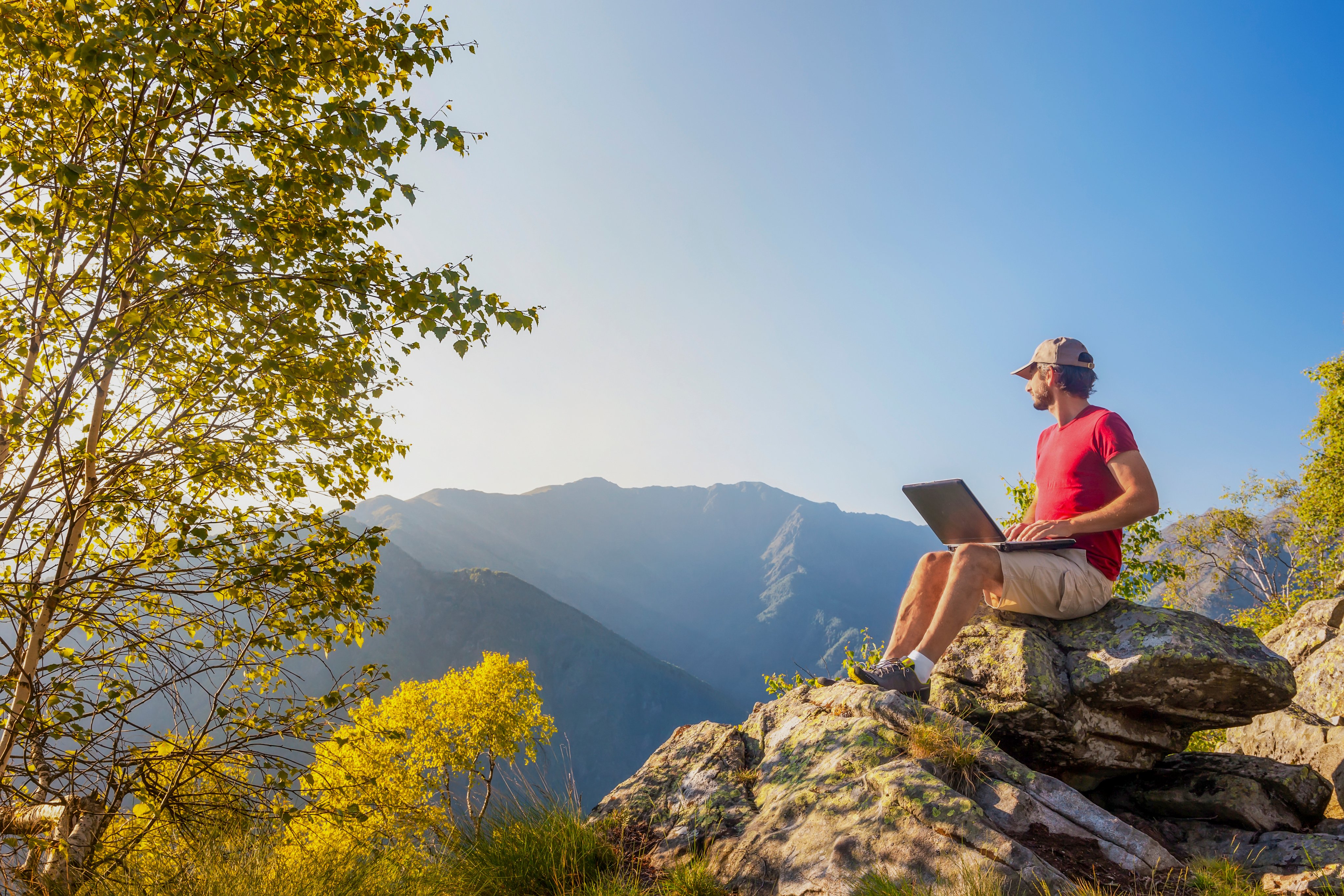 Person sitzt auf Felsen mit Laptop in der Natur und genießt einen Premium Cluburlaub