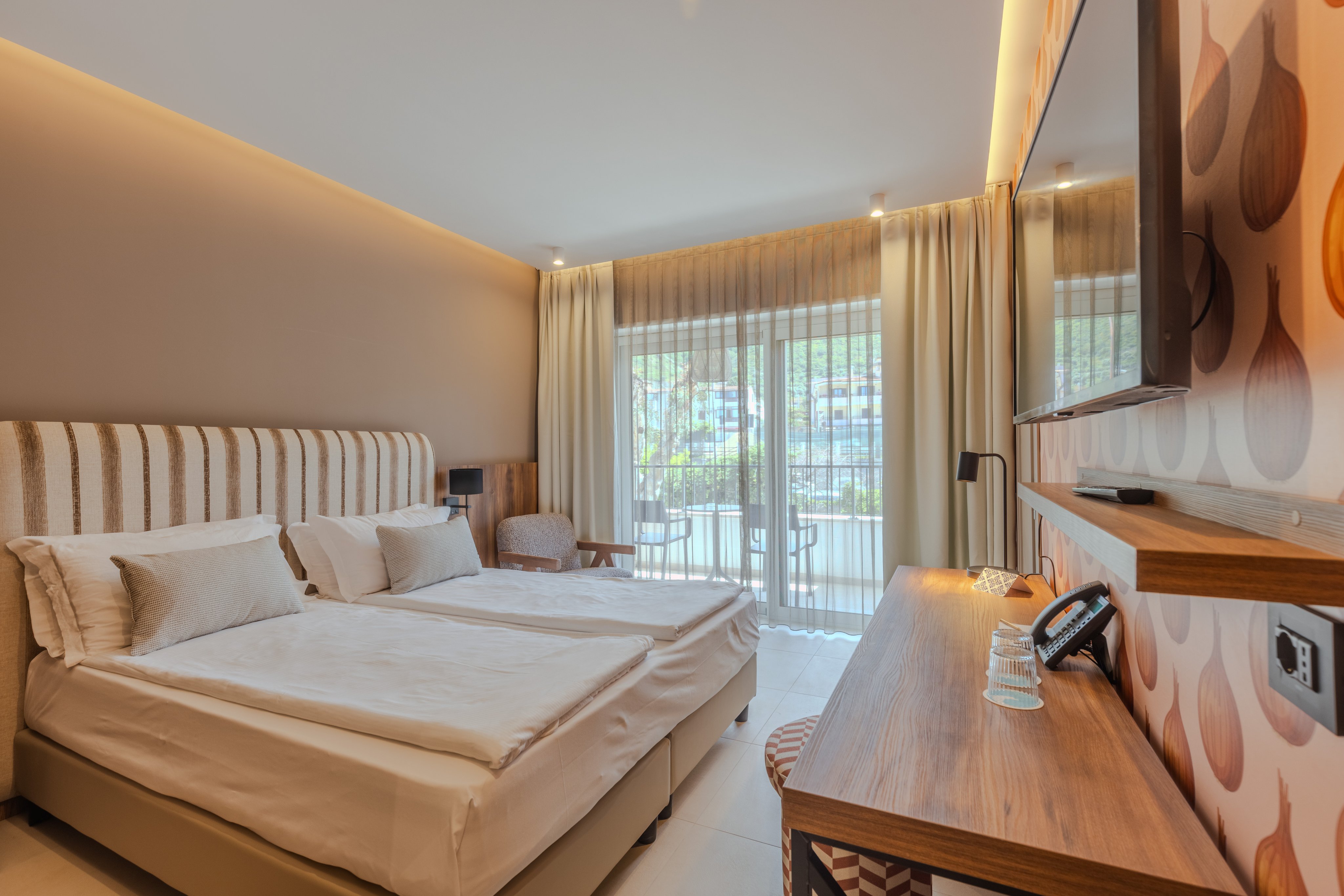 Helles Hotelzimmer mit großem Bett und Blick auf die Terrasse, modern eingerichtet