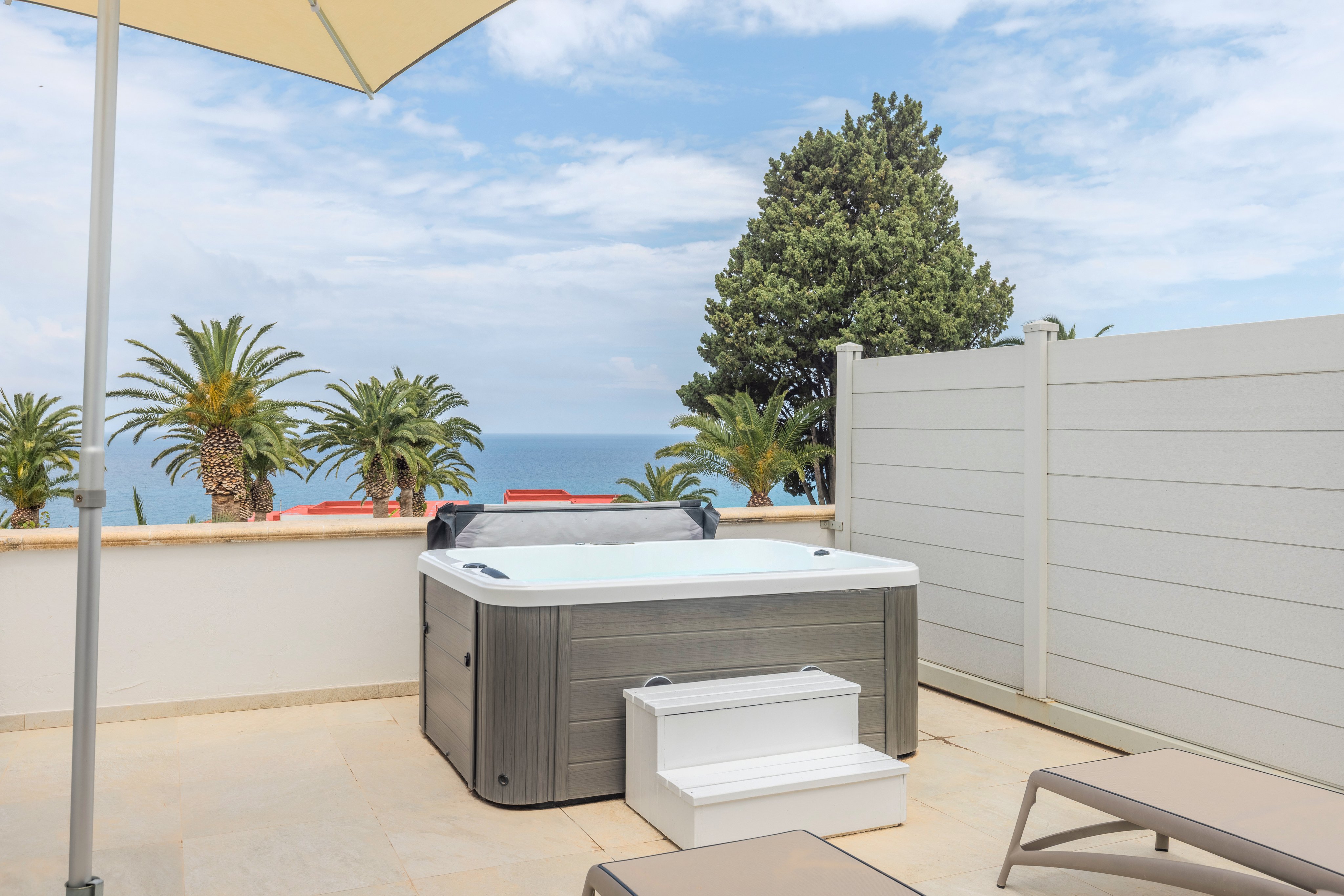 Ein hot tub auf einer Terrasse mit Meerblick, umgeben von Palmen und einem weißen Zaun