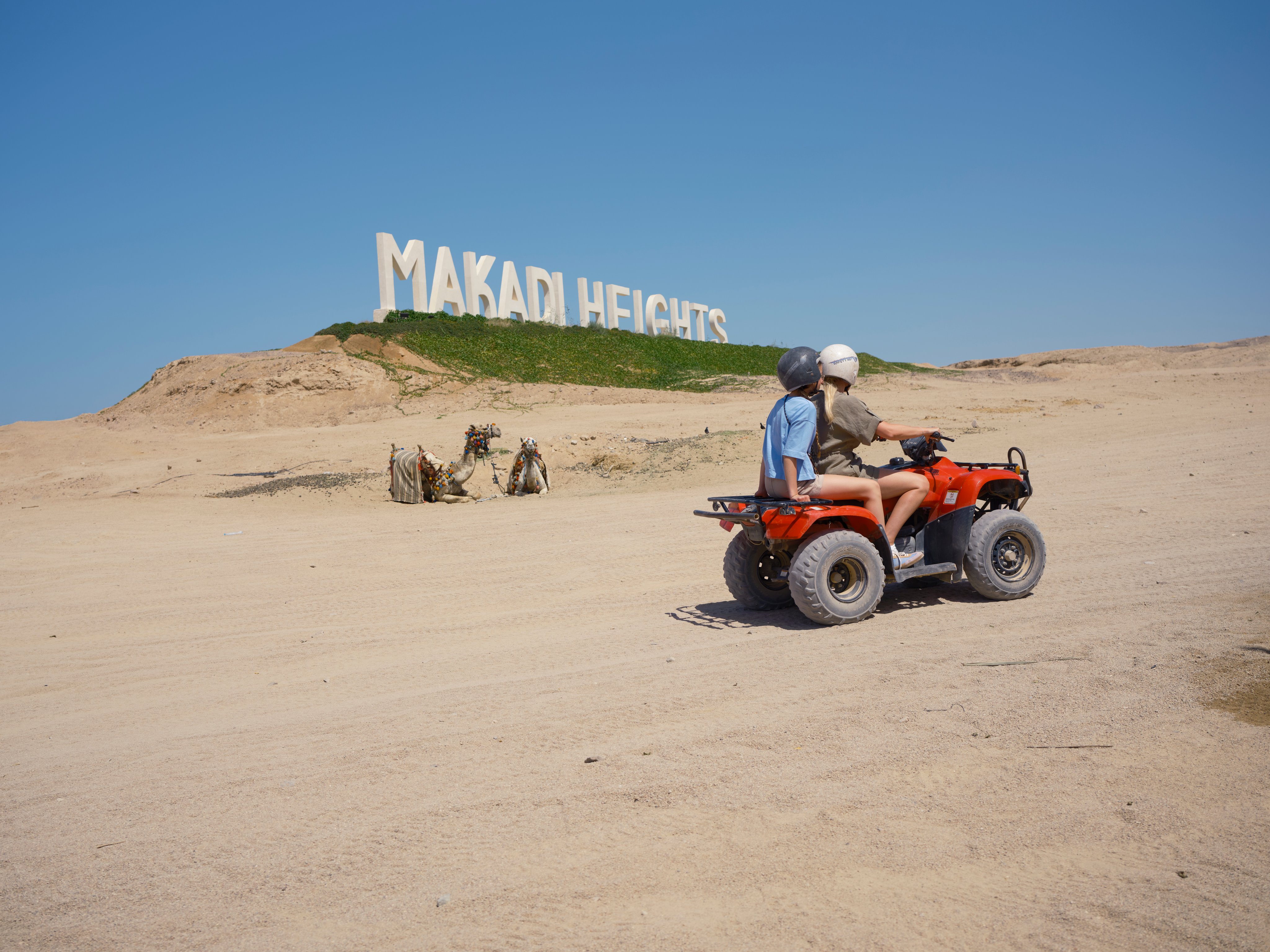 Kinder fahren auf einem Quad in der Wüste vor einem Makadi Heights Schild bei Aldiana Premium Cluburlaub