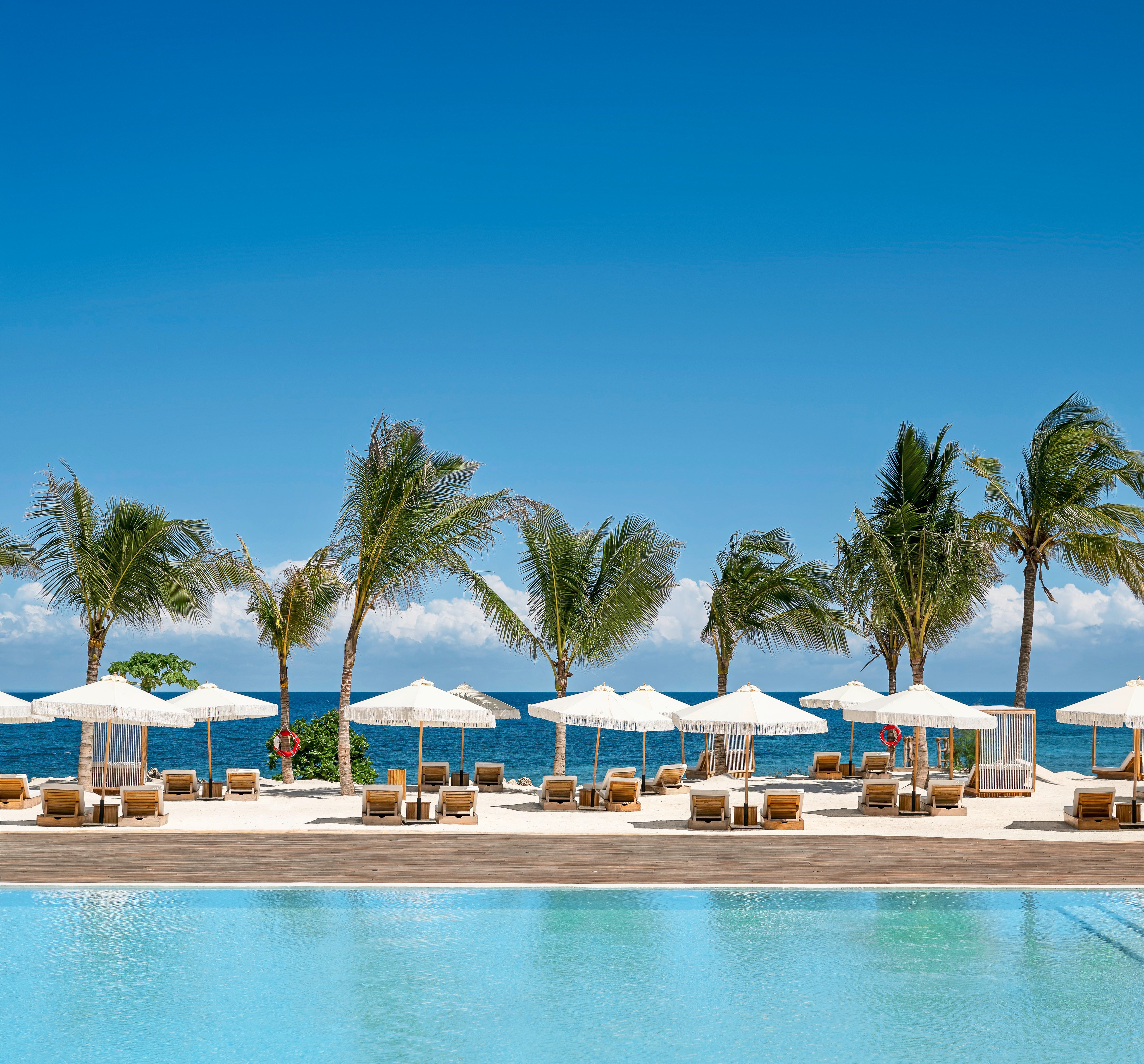 Blick auf den Poolbereich bei Aldiana mit Palmen, Sonnenschirmen und Liegen am Strand