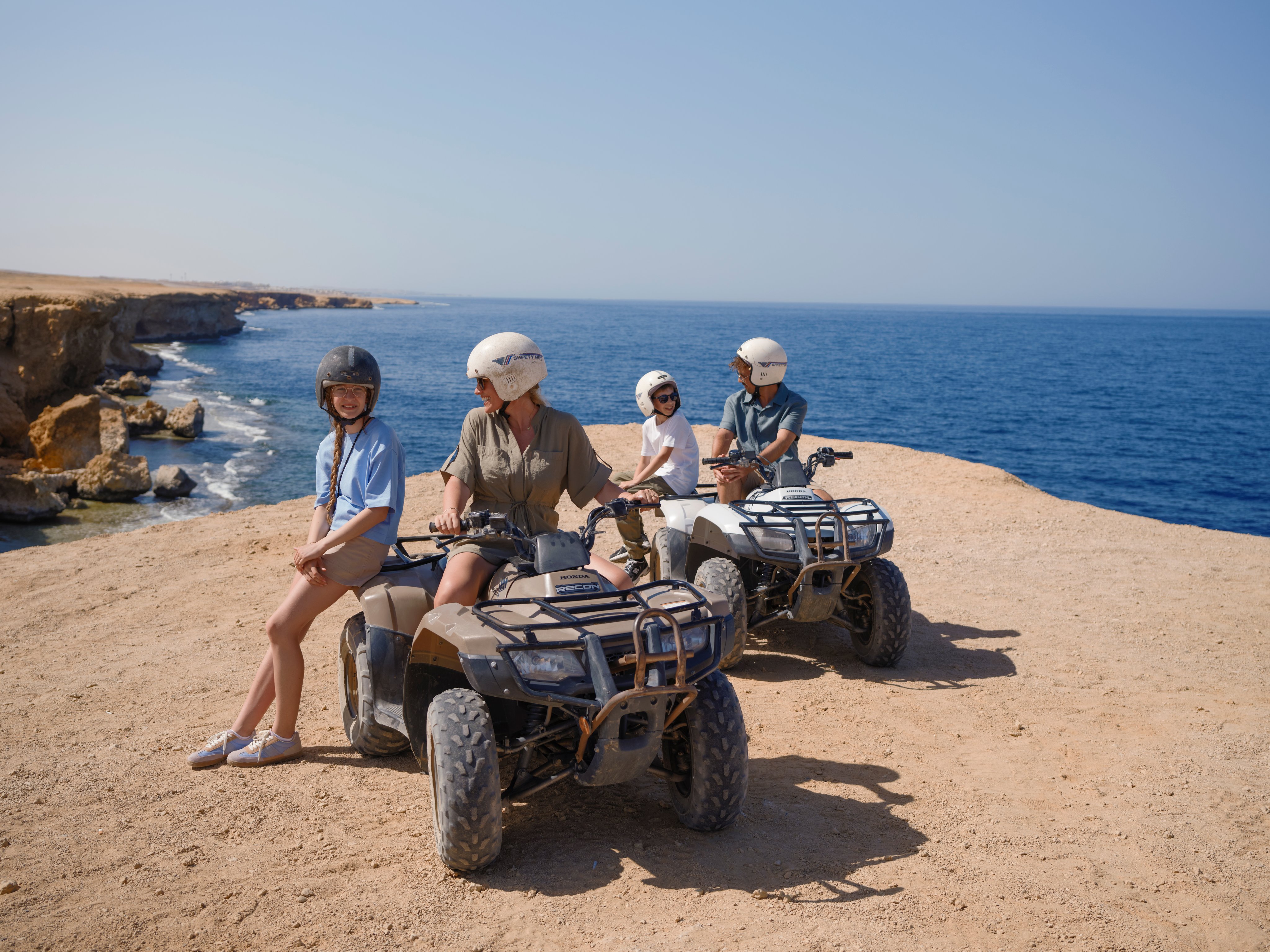 Vier Kinder fahren mit Quadbikes am Strand bei Sonnenlicht auf einem Urlaubsplatz