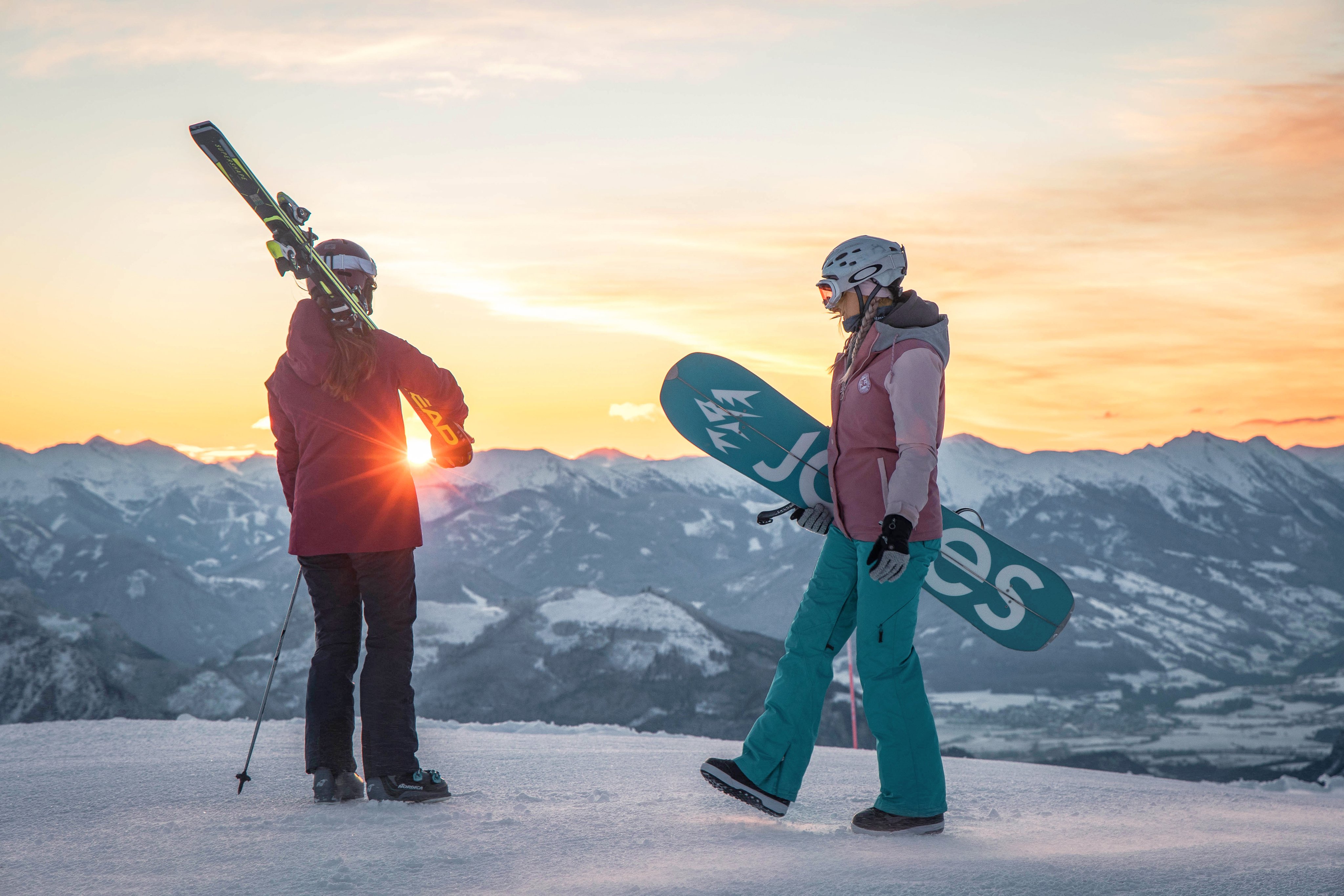 Zwei Skifahrer auf schneebedecktem Gipfel mit Bergpanorama bei Sonnenuntergang