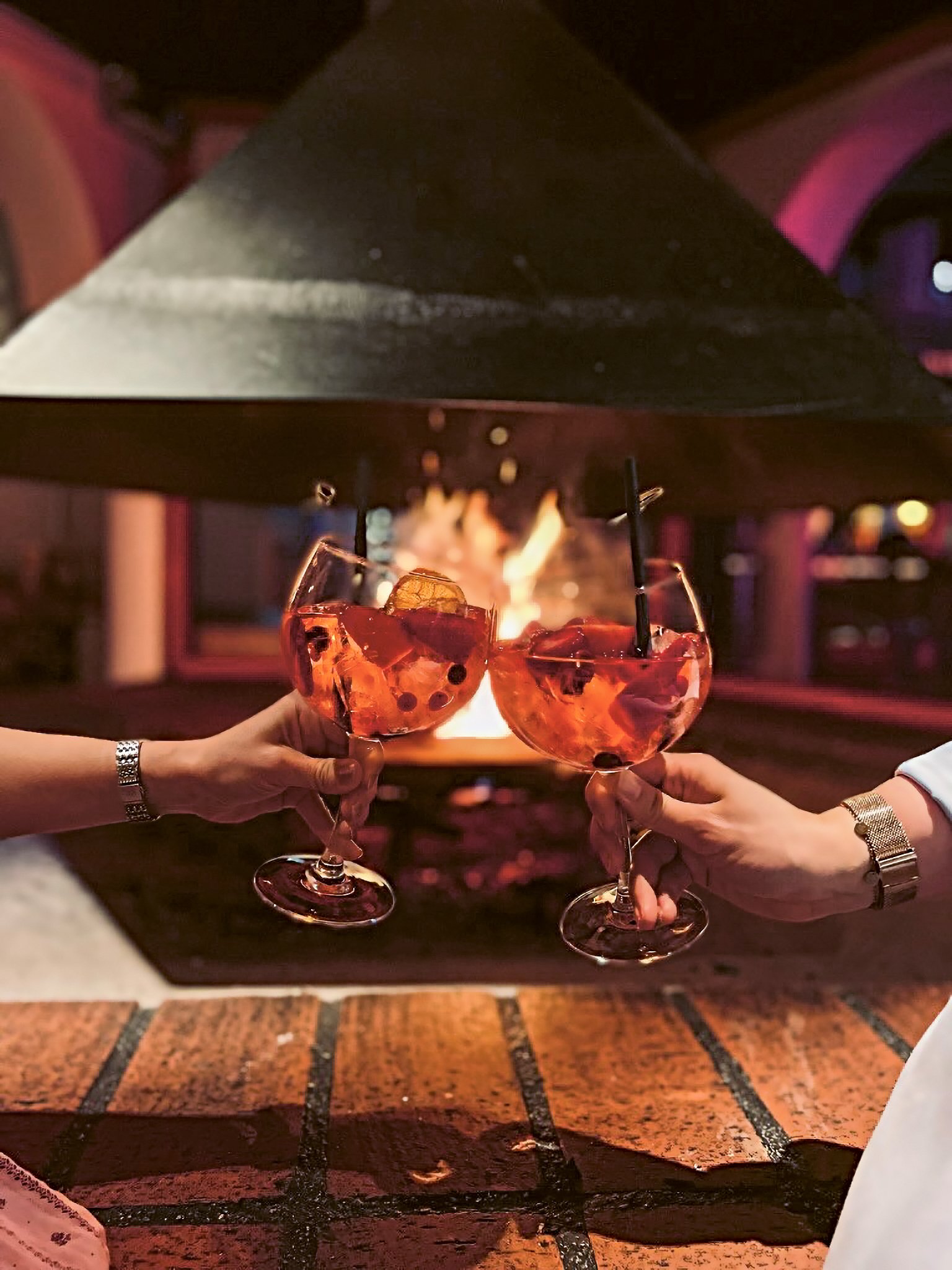 Zwei Personen stoßen mit Rotweingläsern an, gemütliche Atmosphäre am Kamin bei Aldiana