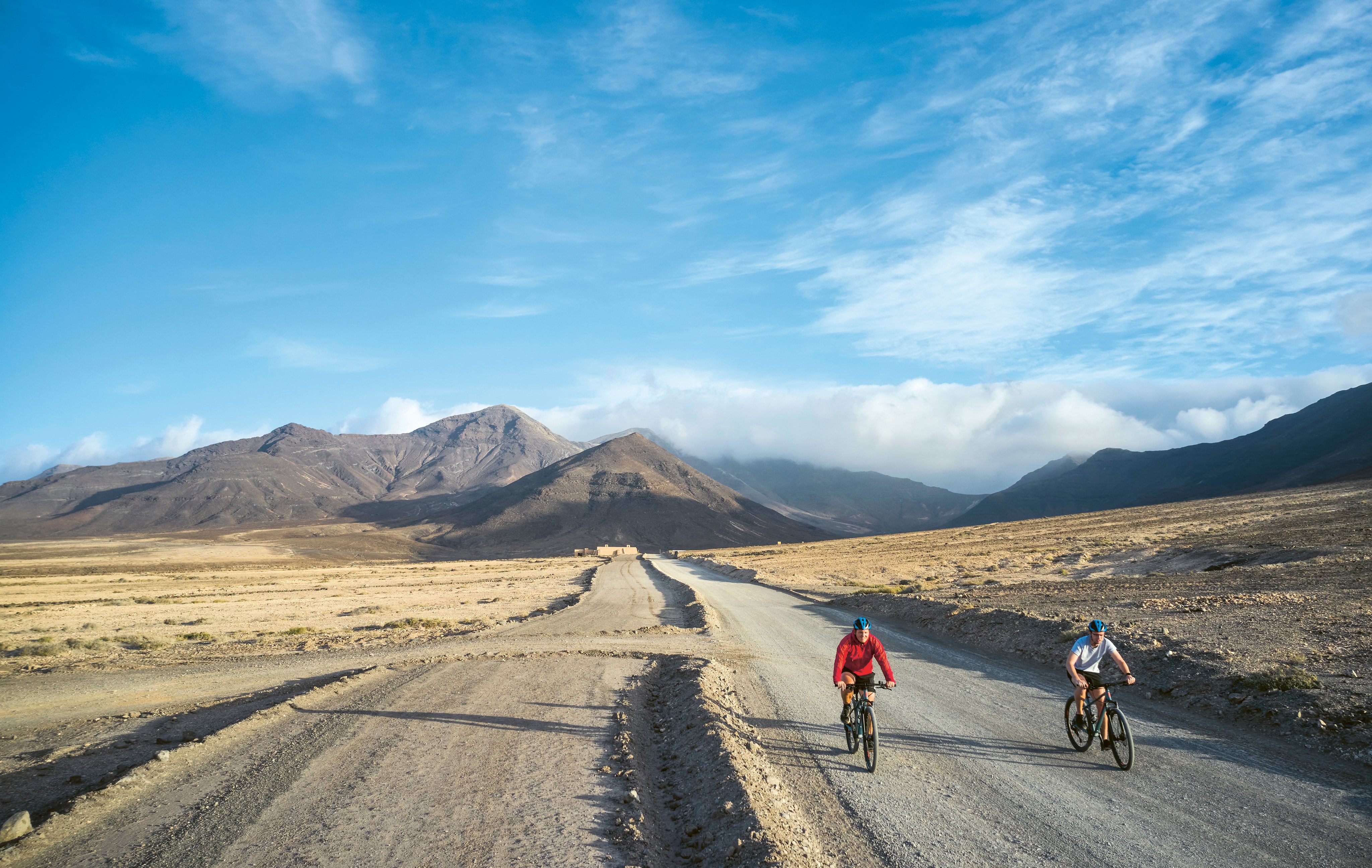Zwei Radfahrer auf einer unbefestigten Straße in einer Berglandschaft bei Sonnenlicht
