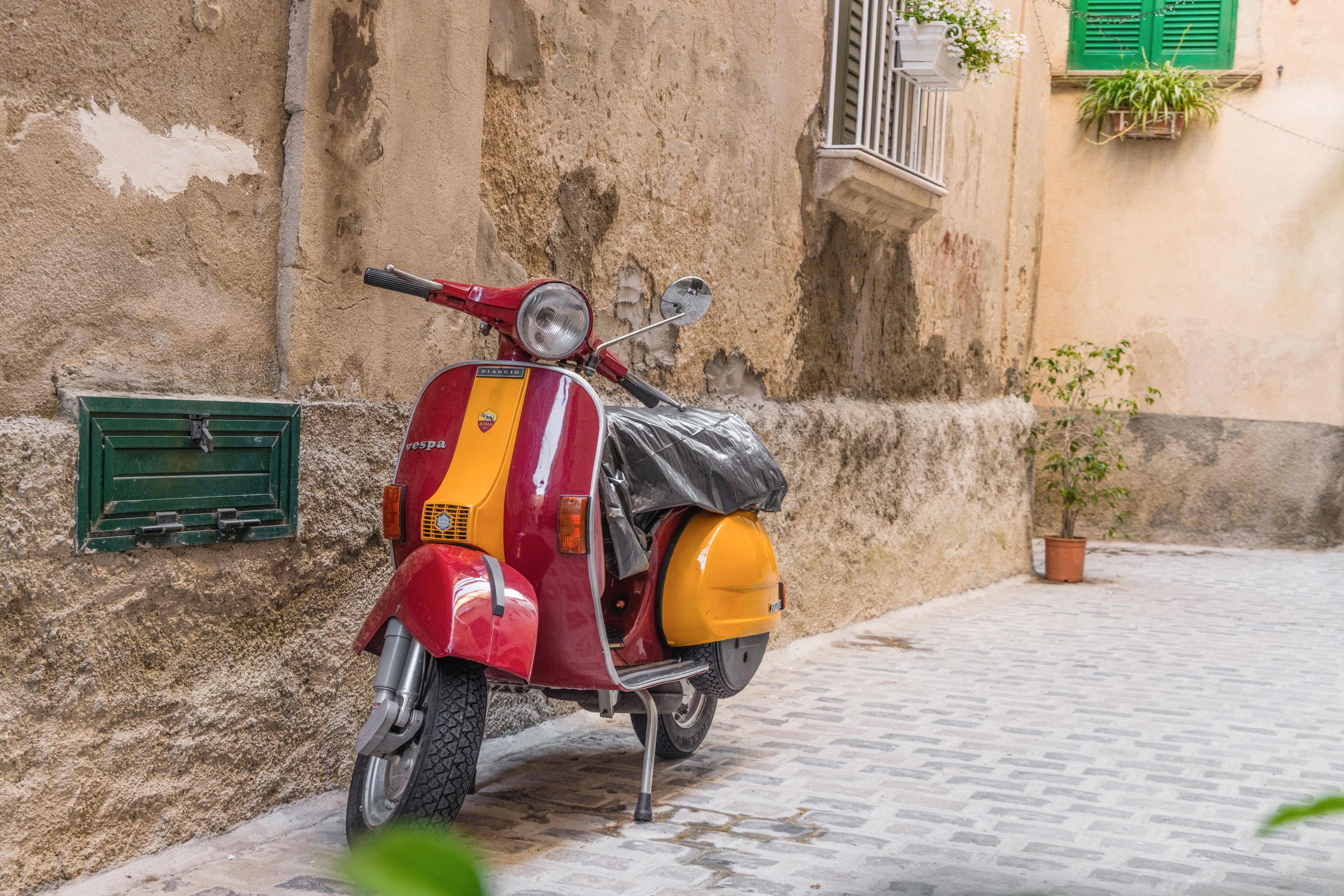 Ein roter und gelber Motorroller vor einer alten Hauswand, ruhend auf Kopfständer