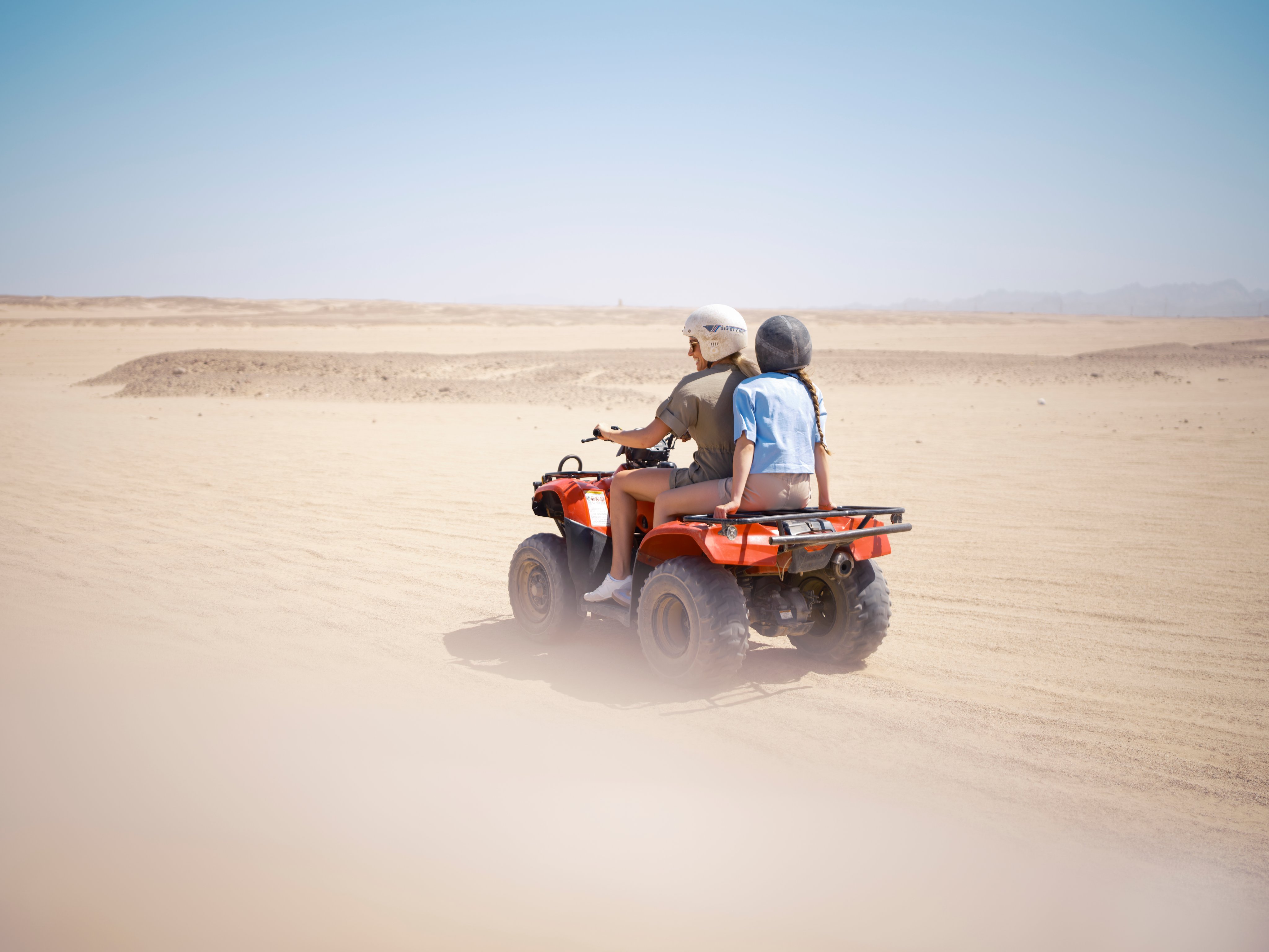 Personen fahren auf einem Quad durch den Sand in einer Wüstenlandschaft