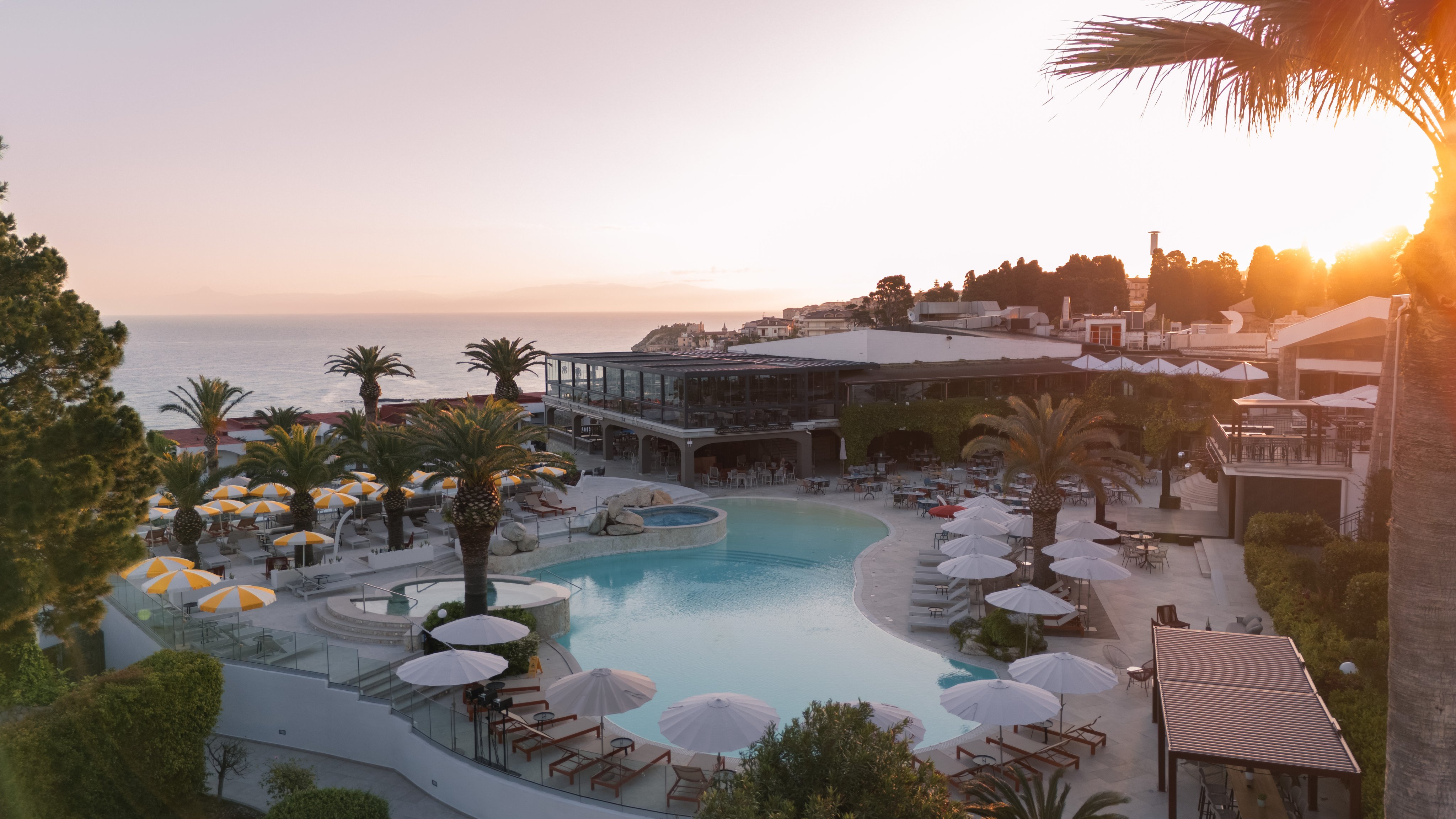 Blick auf den Poolbereich eines Aldiana Premium Clubs mit Palmen und Sonnenuntergang