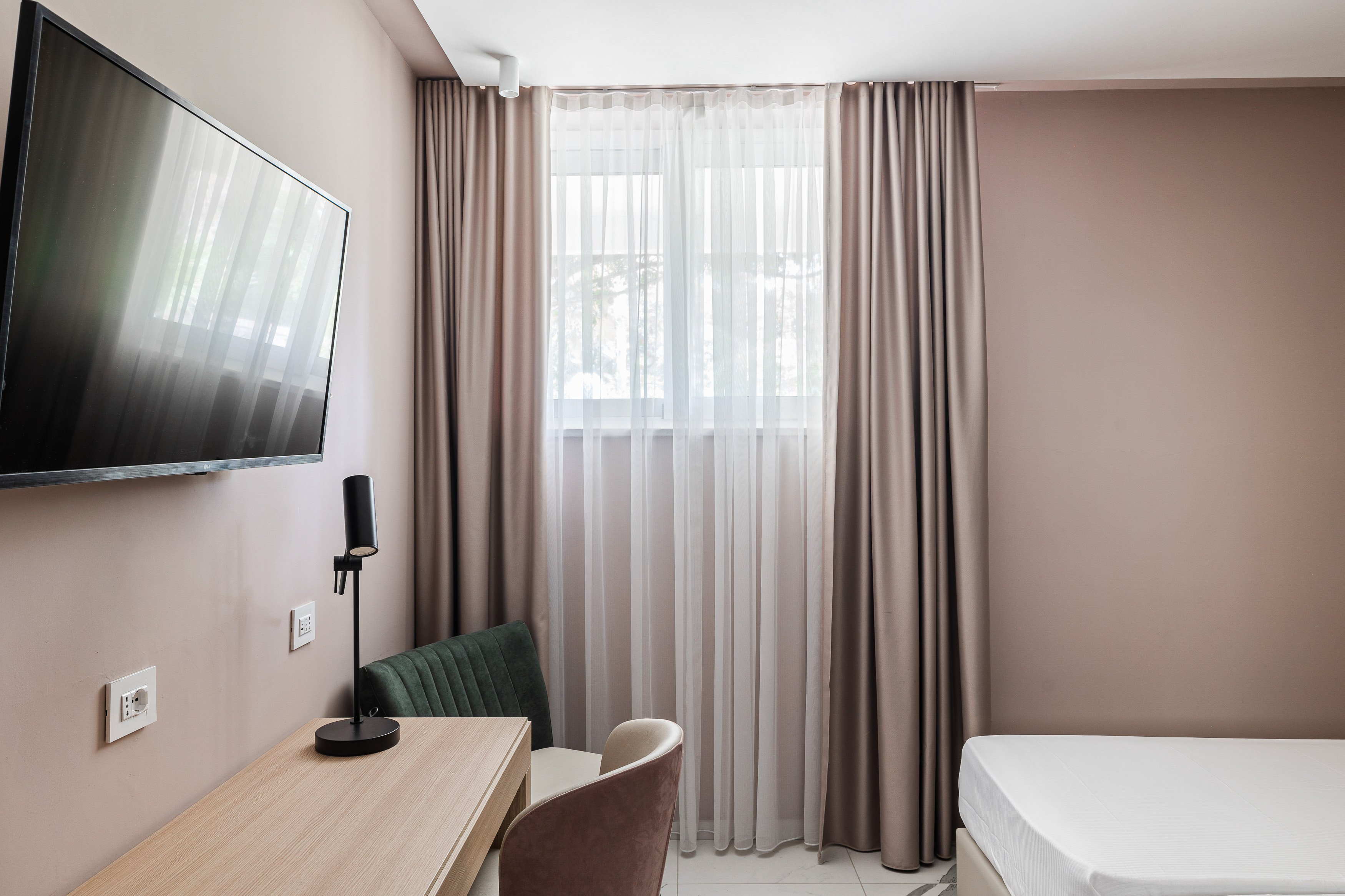 Elegantes Hotelzimmer mit Bett, Schreibtisch, Stuhl, Fernseher und Fenster mit Vorhängen