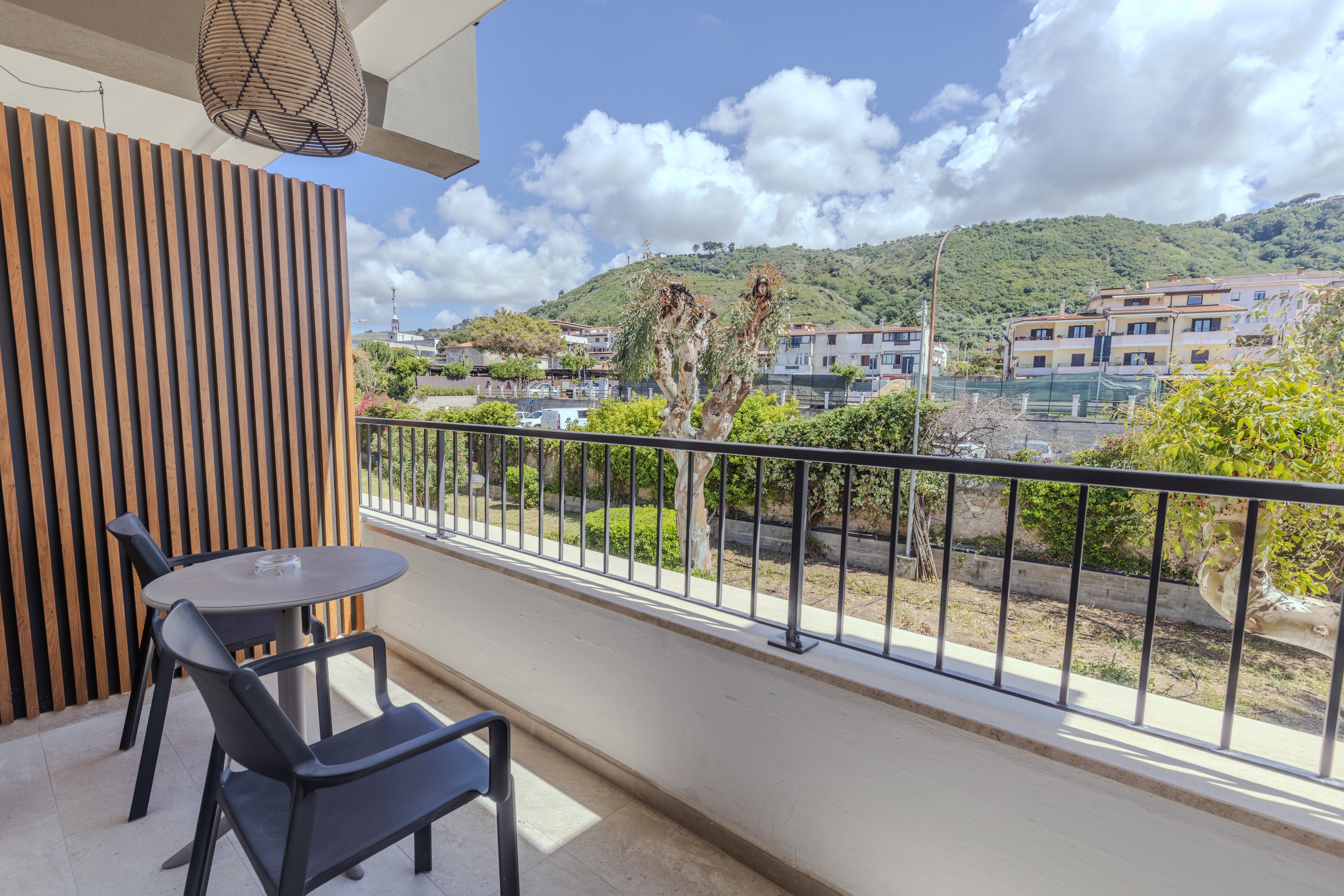 Balkon mit Blick auf grüne Hügel und Häuser, Sitzgelegenheiten, sonniger Tag