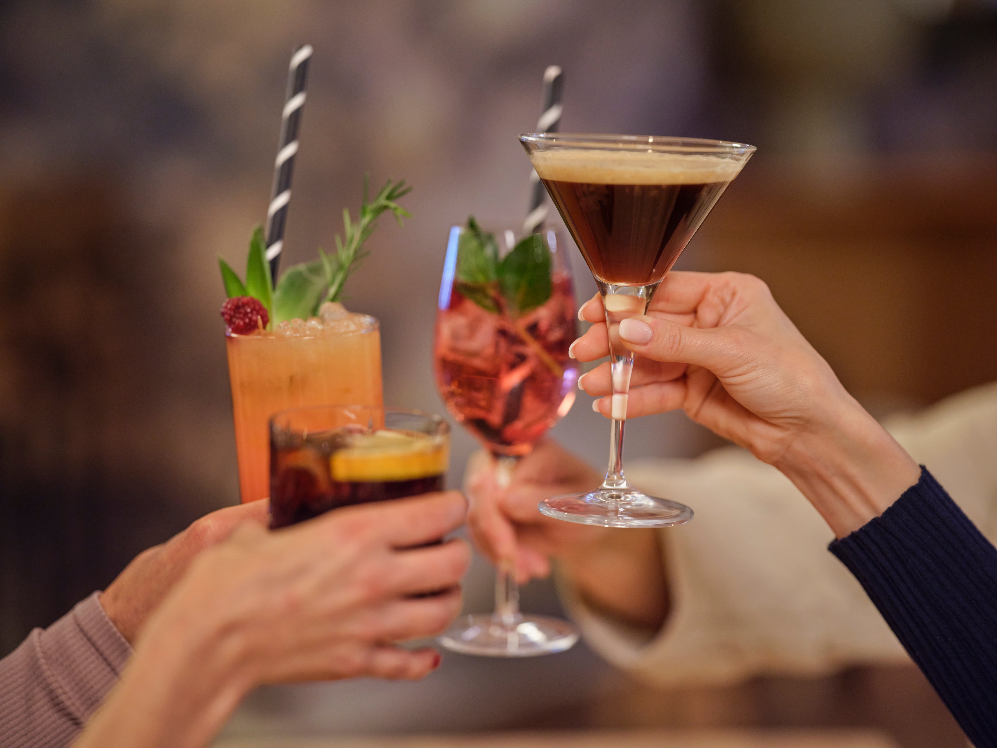 Drei Menschen stoßen mit bunten Cocktails in einer eleganten Bar an