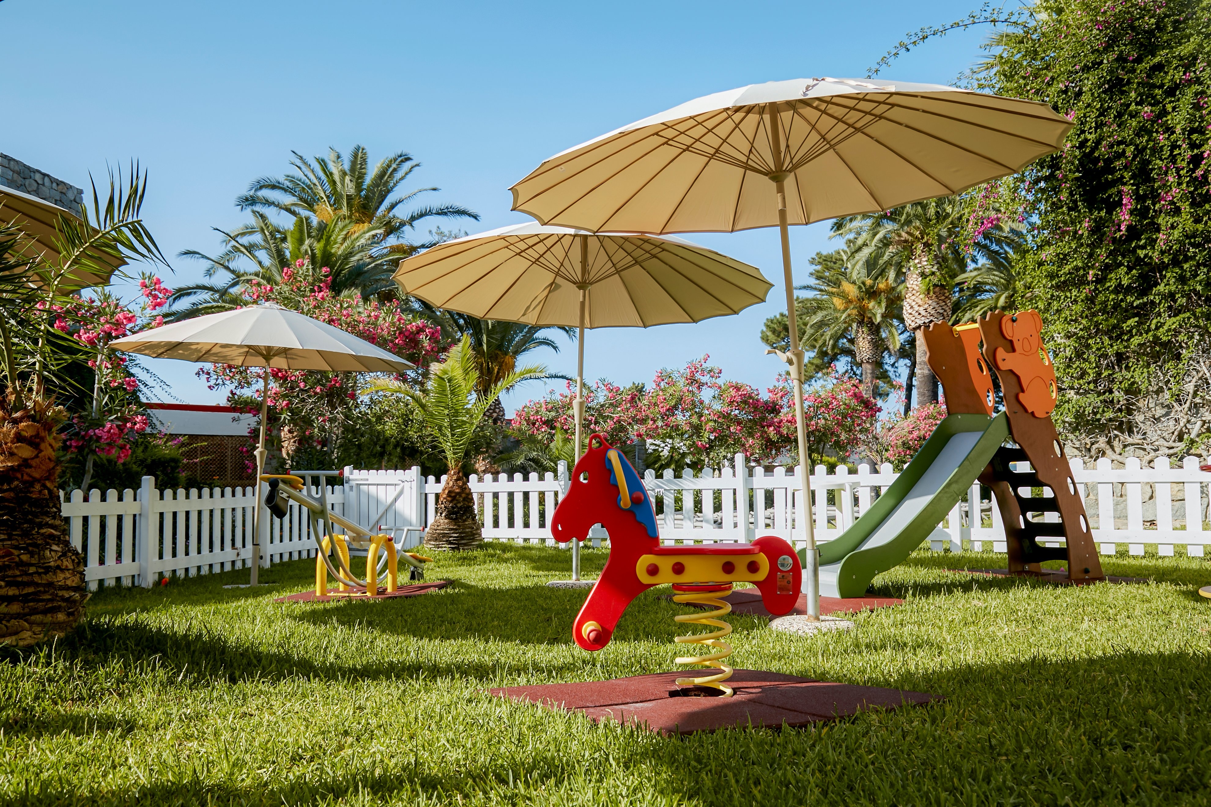 Kinder-Spielplatz mit Schaukeln, Rutsche und Sonnenschirmen im gepflegten Garten