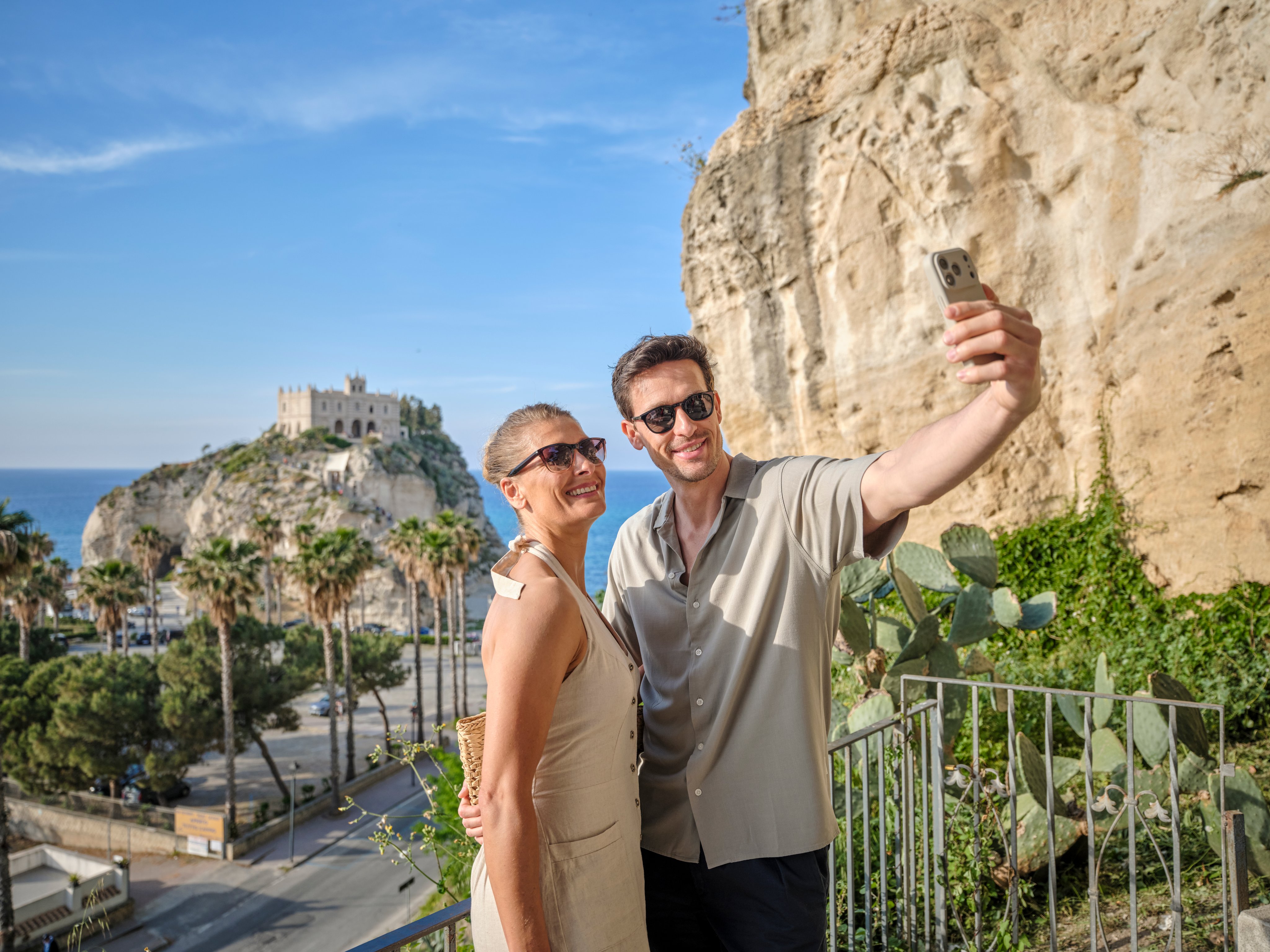 Zwei Personen machen Fotos vor Felsen mit Blick auf eine Küste und einen historischen Turm