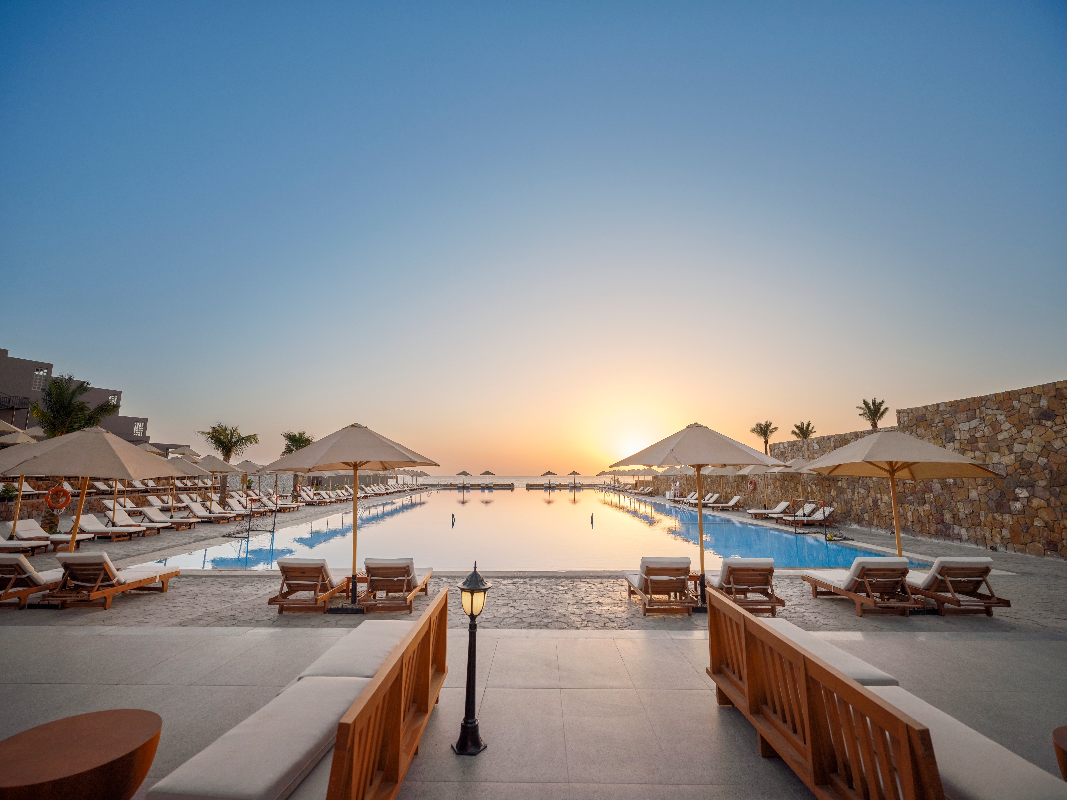 Traumhafte Hotelanlage am Strand mit Pool, Liegen und Sonnenschirmen bei Sonnenuntergang