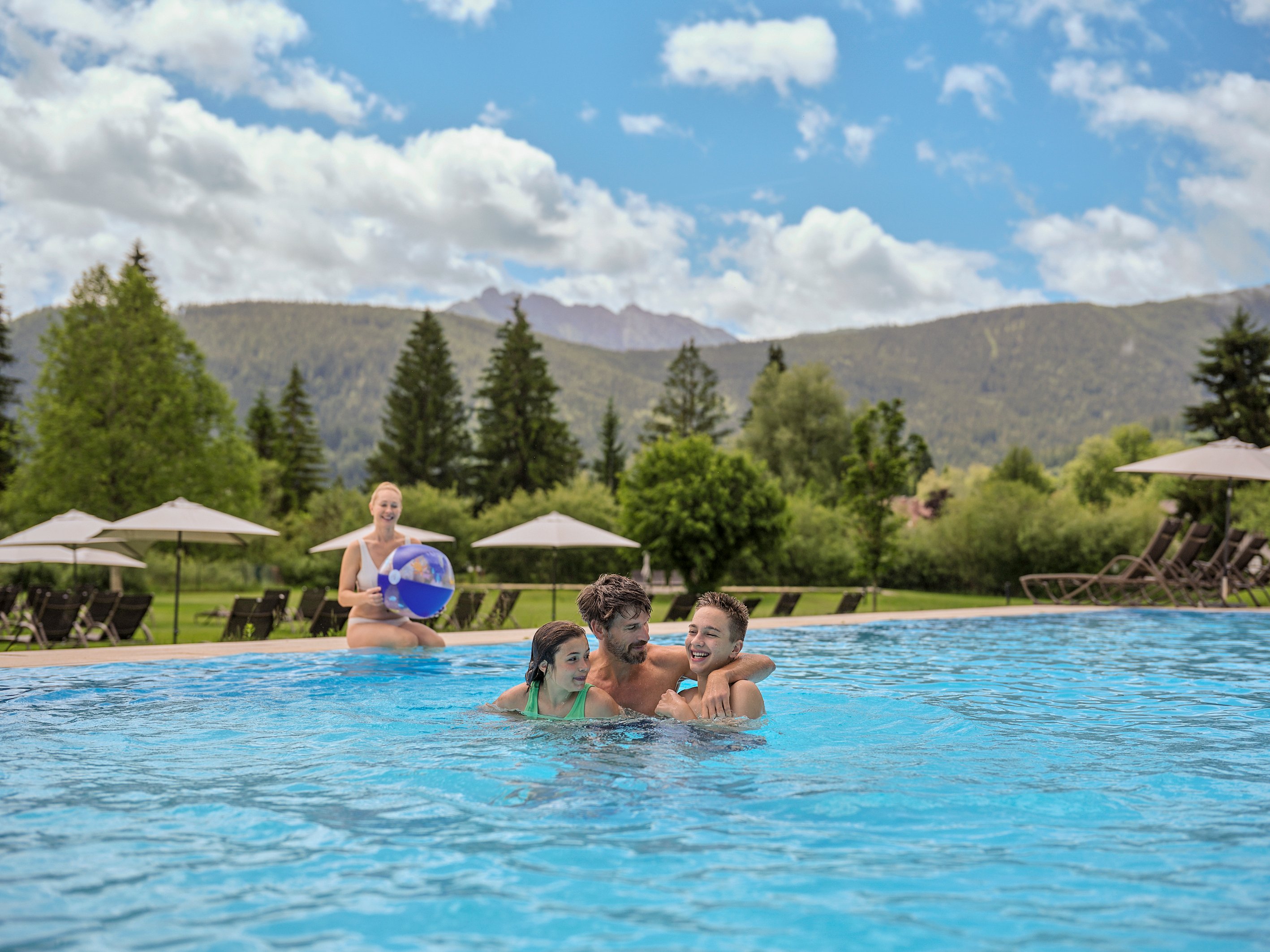 Familie beim Schwimmen im Pool vor Bergen und grüner Landschaft bei Aldiana