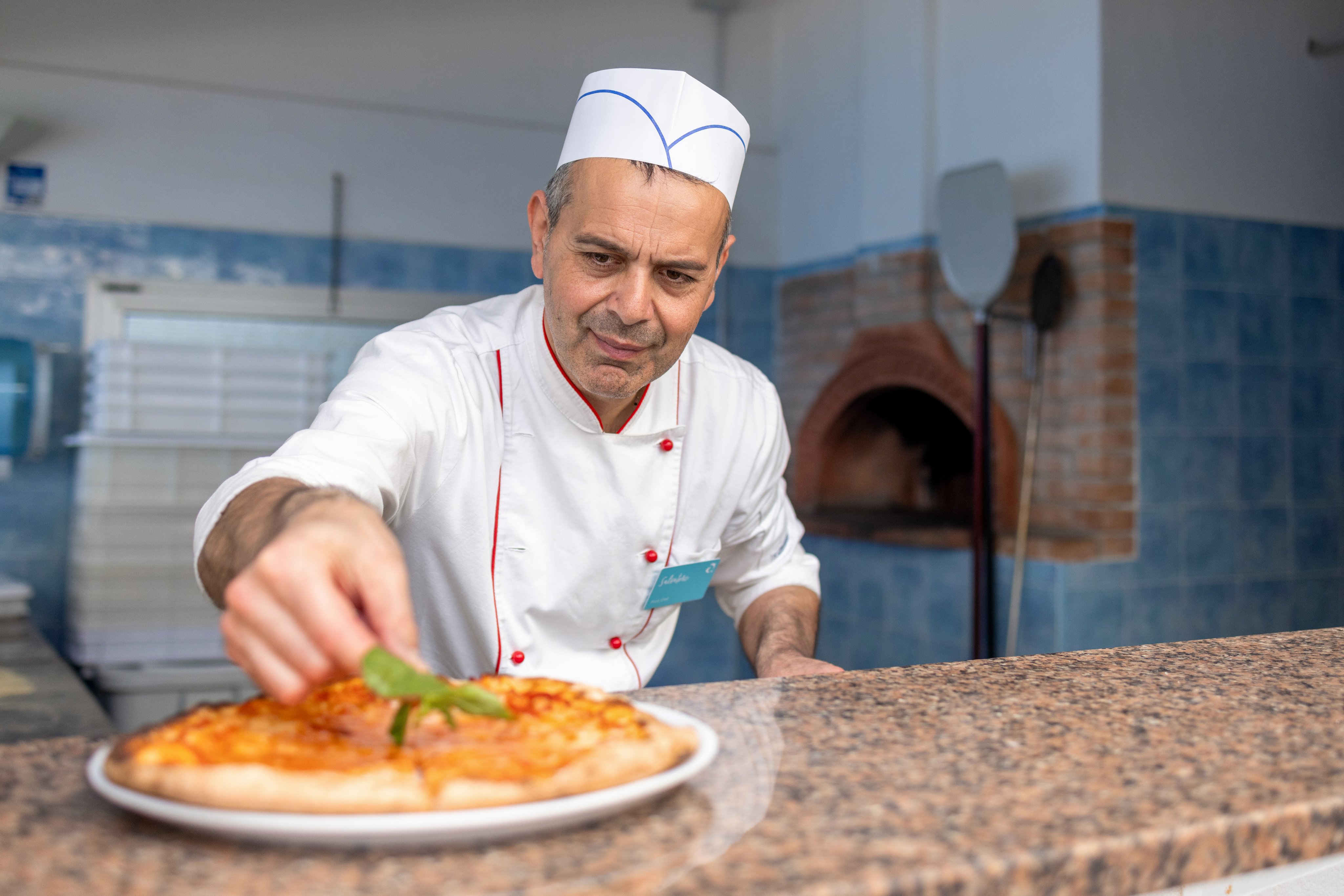 Koch in einer professionellen Küche bereitet eine Pizza im Premium Cluburlaub bei Aldiana zu