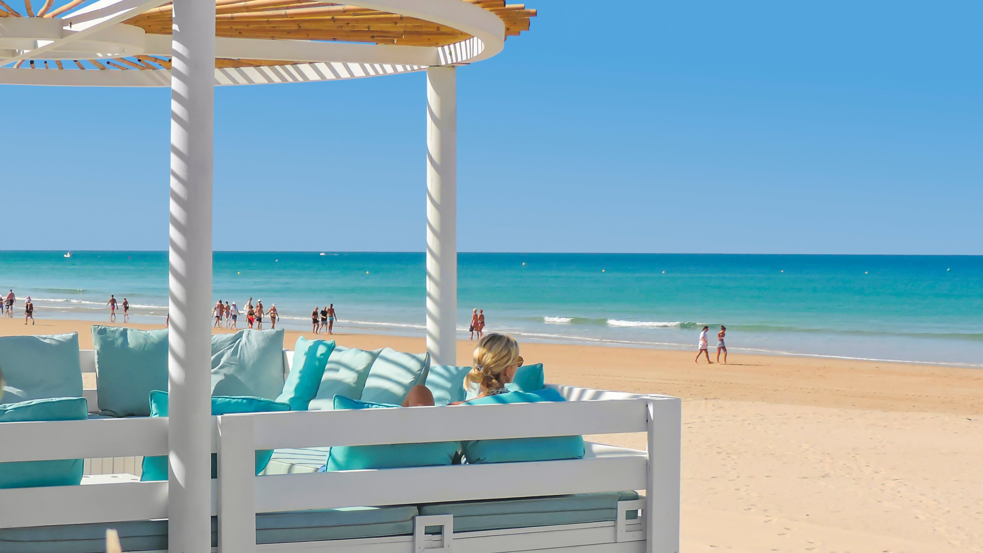 Sunny beach with white sand, blue sea, umbrellas, and relaxing guests at a premium Aldiana club