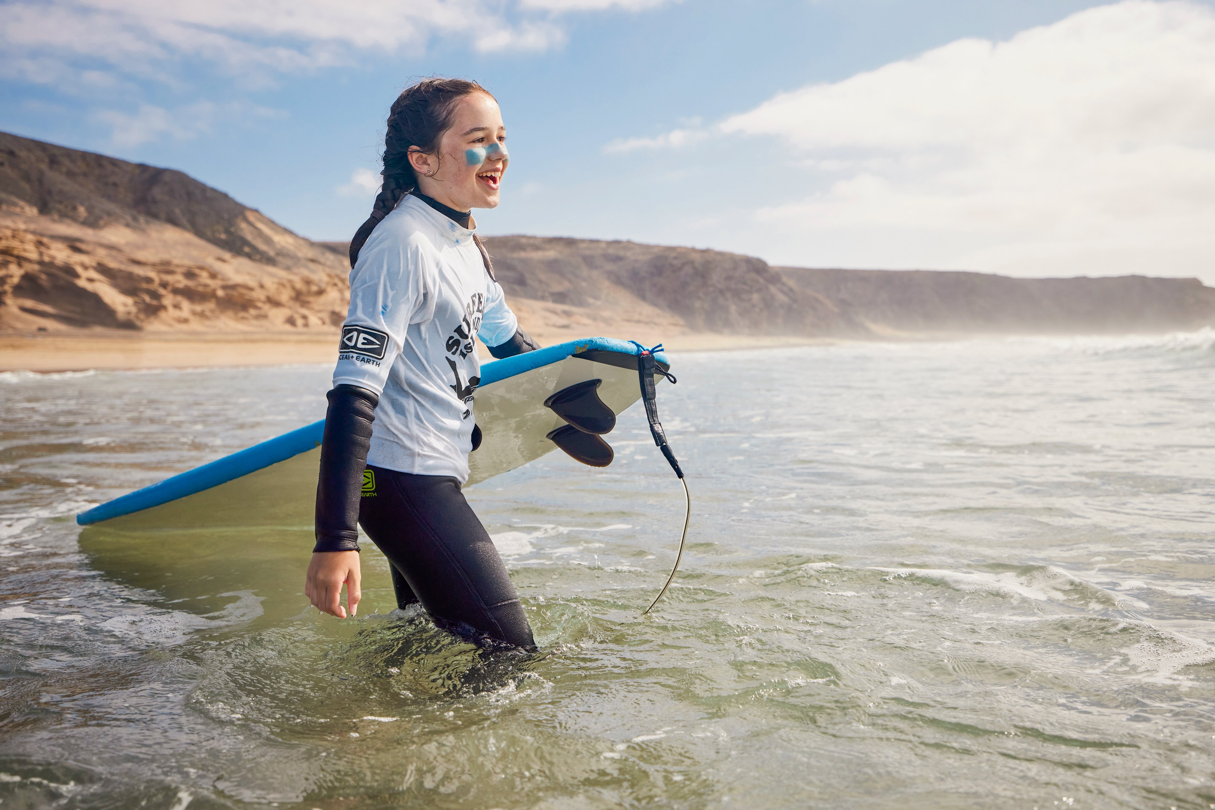 Jugendlicher mit Surfbrett beim Schnorcheln am Strand, bei Sonnenaufgang in alpenähnlicher Küstenlandschaft