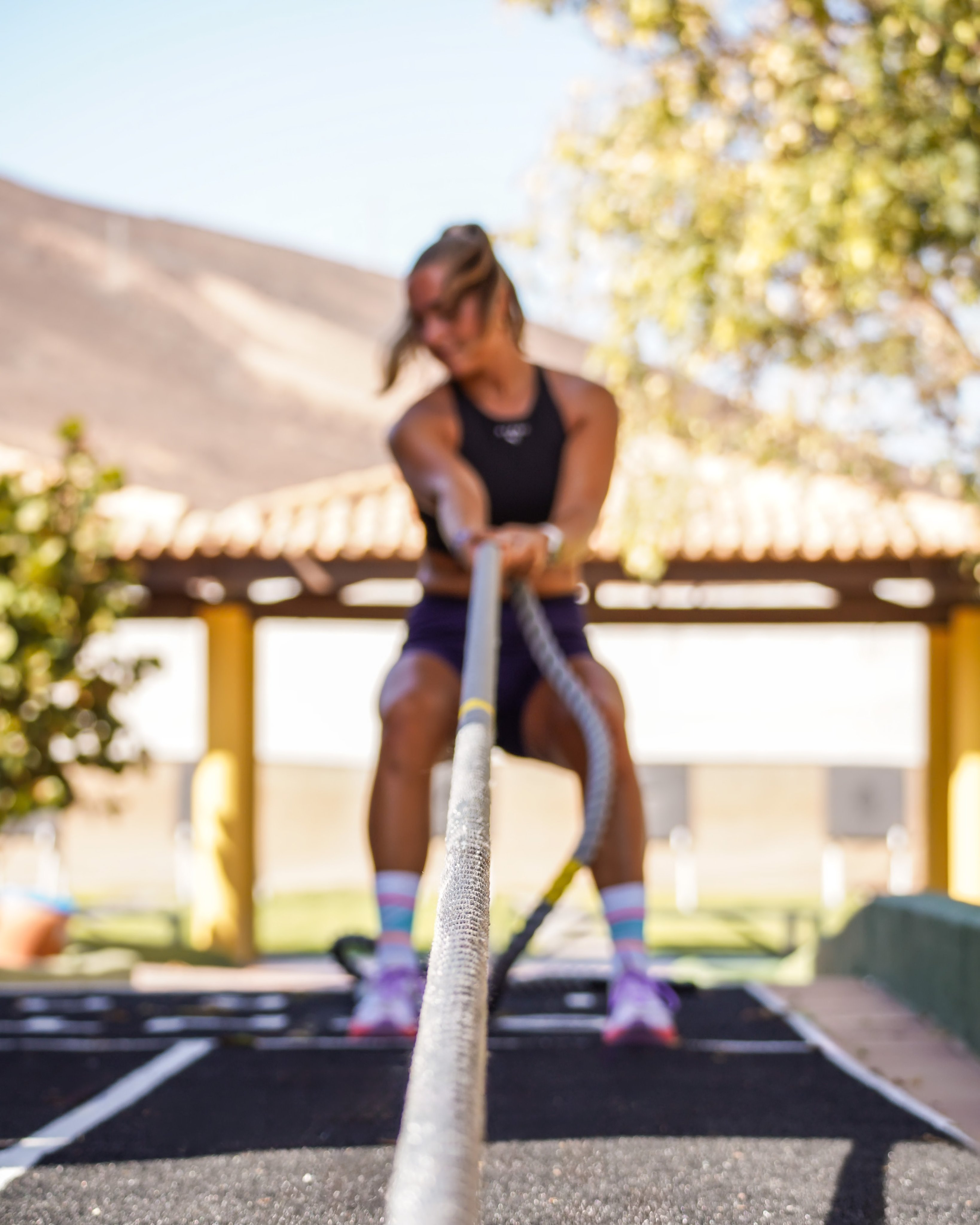 Eine Frau trainiert mit einem Seil im Freien auf einem Sportplatz, Sonnenschein.