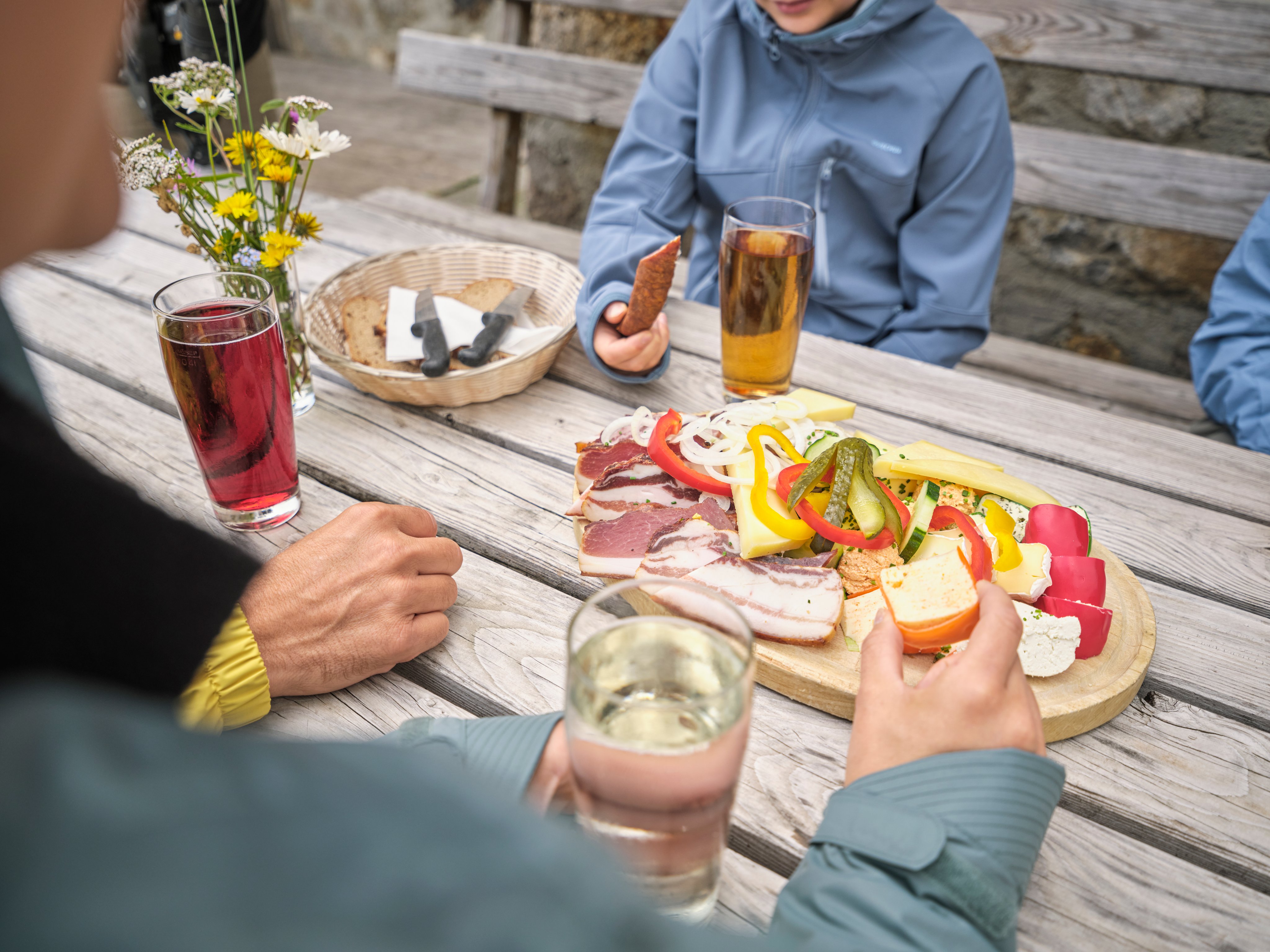 Familien beim Picknick im Freien mit bunten Lebensmitteln und Getränken auf Holzbank