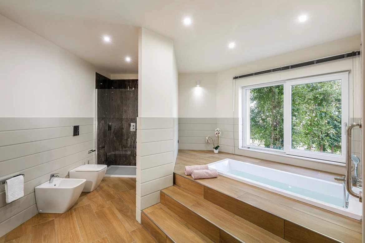 Ein modernes Badezimmer mit Dusche, Badewanne und Blick auf grüne Natur, ideal für Premium Urlaub bei Aldiana