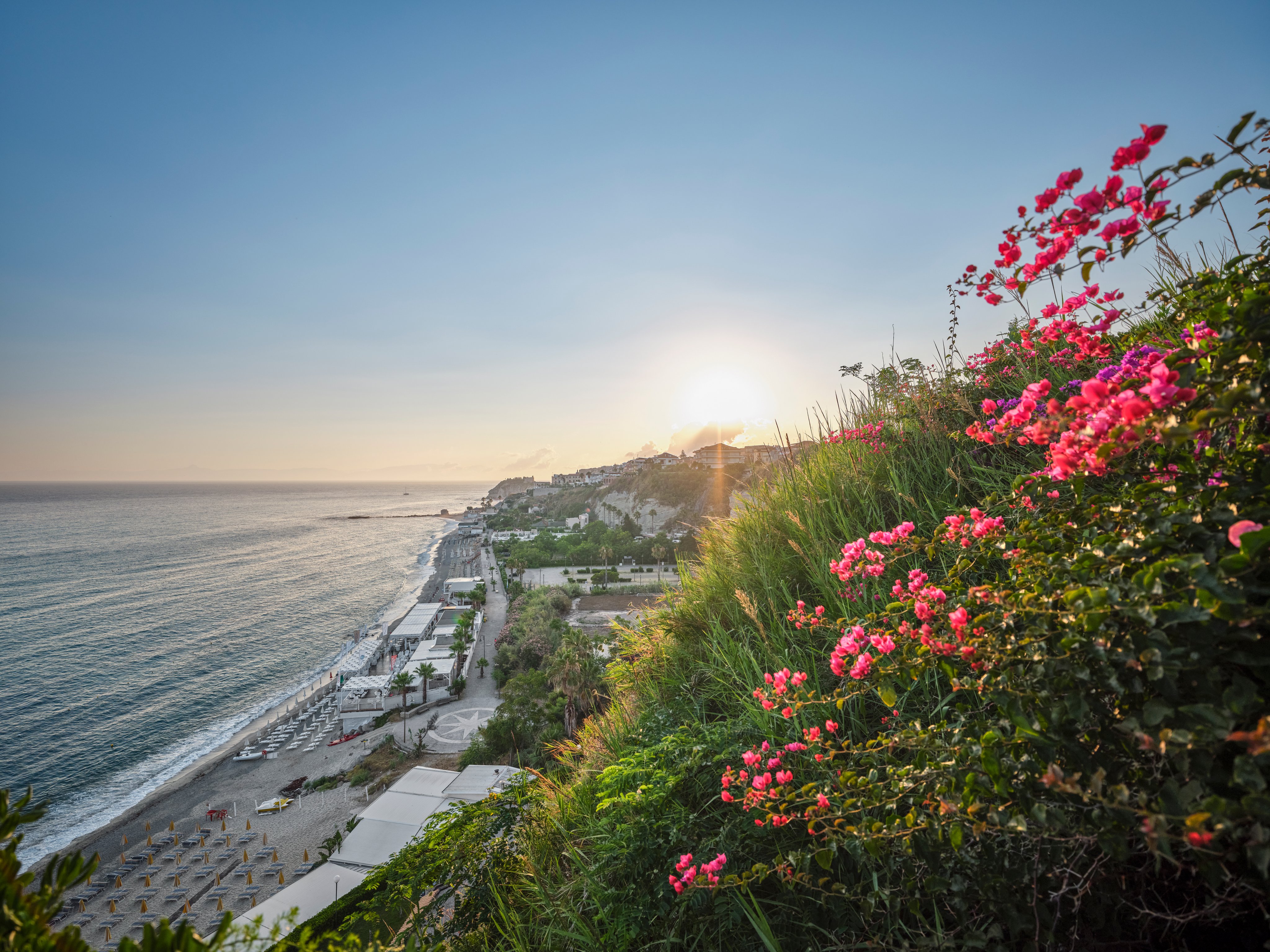 Blick auf die Küste bei Sonnenuntergang mit Blüten im Vordergrund für Aldiana Premium Cluburlaub