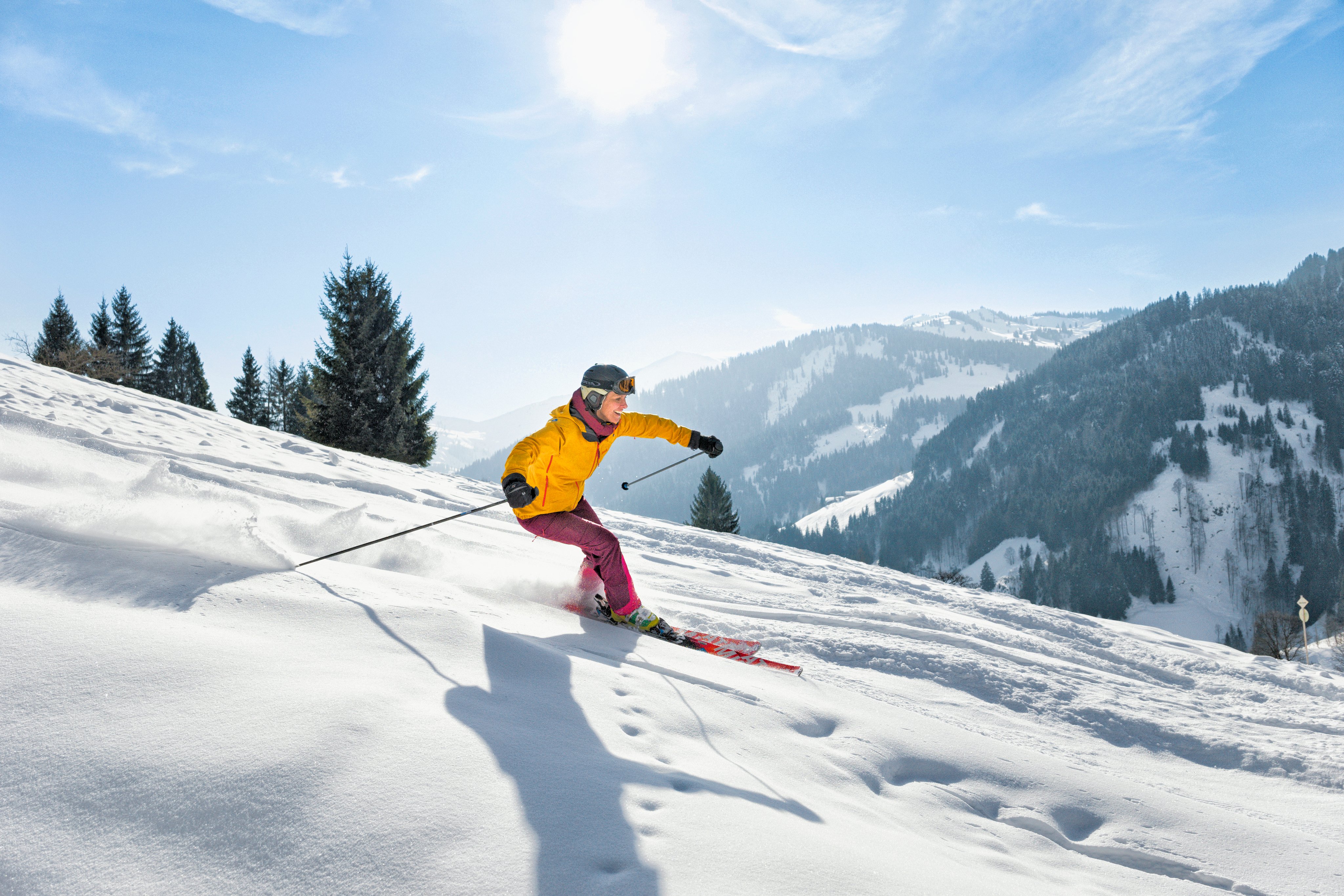 Skifahrerin in gelber Jacke und pinken Hosen auf schneebedeckter Piste in Bergen