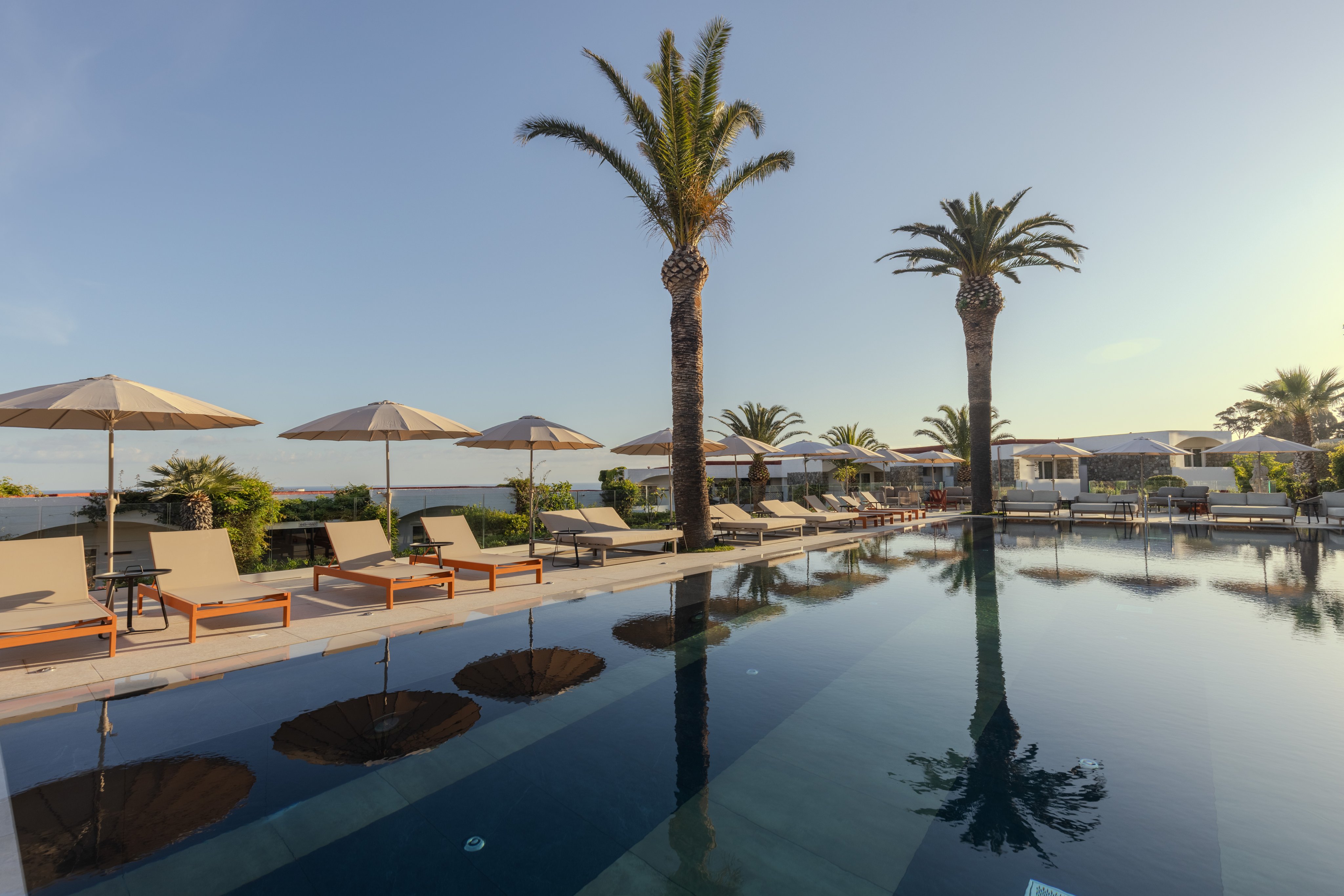 Ein luxuriözer Poolbereich mit Liegen, Sonnenschirmen und Palmen am Meer bei Aldiana