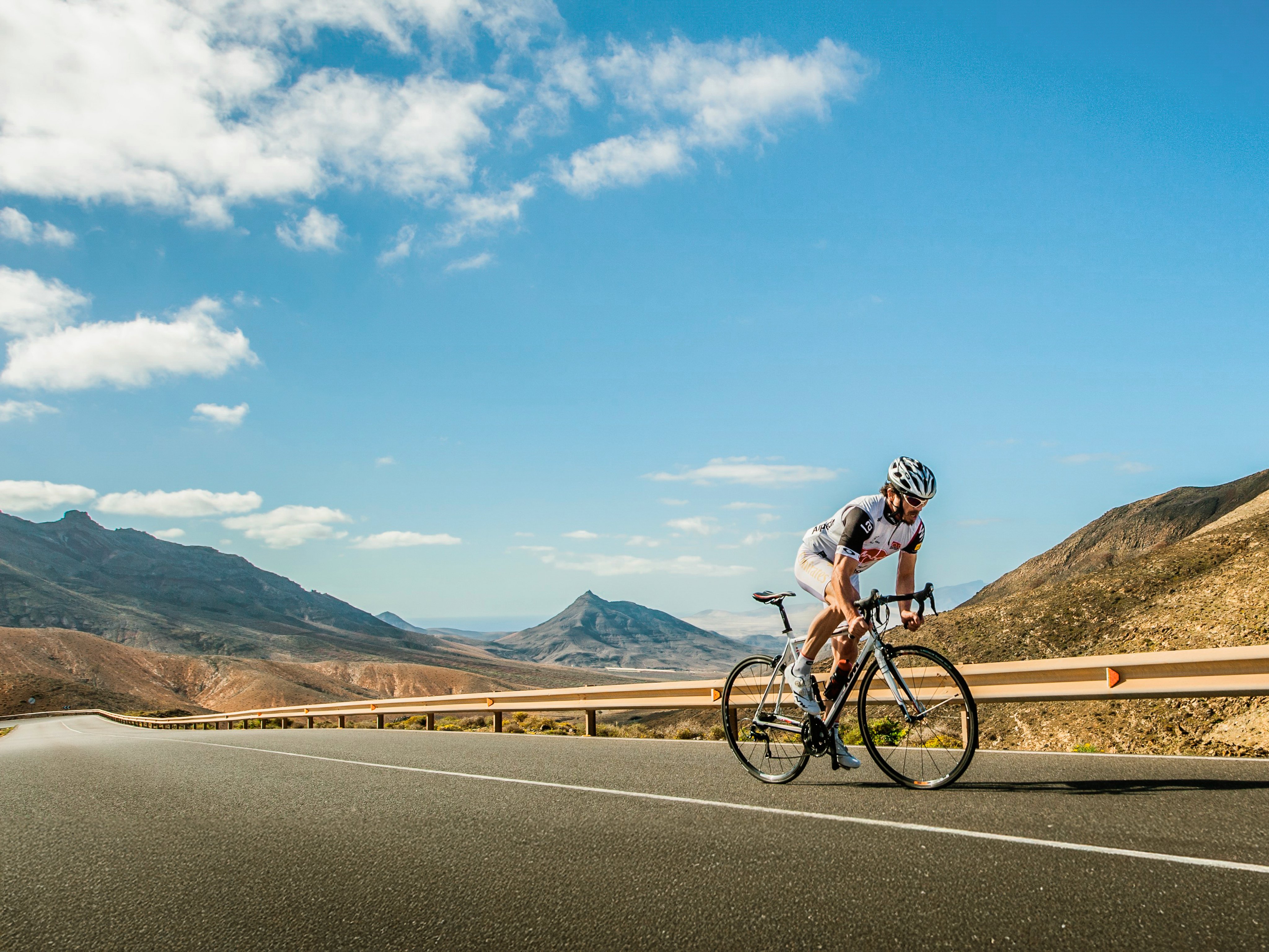 Ein Radfahrer fährt auf einer kurvigen Straße durch eine sonnige Berglandschaft.