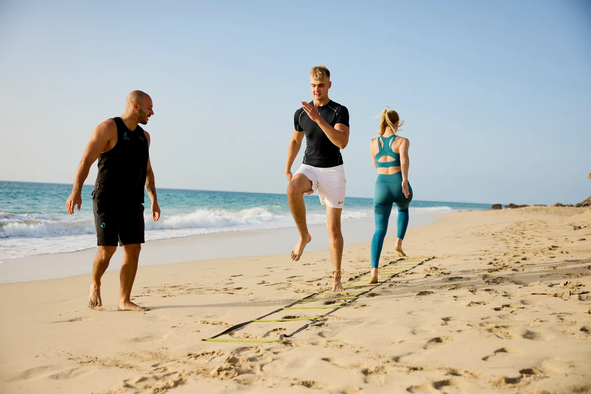 2 Personen mit Trainer am Strand beim Workout