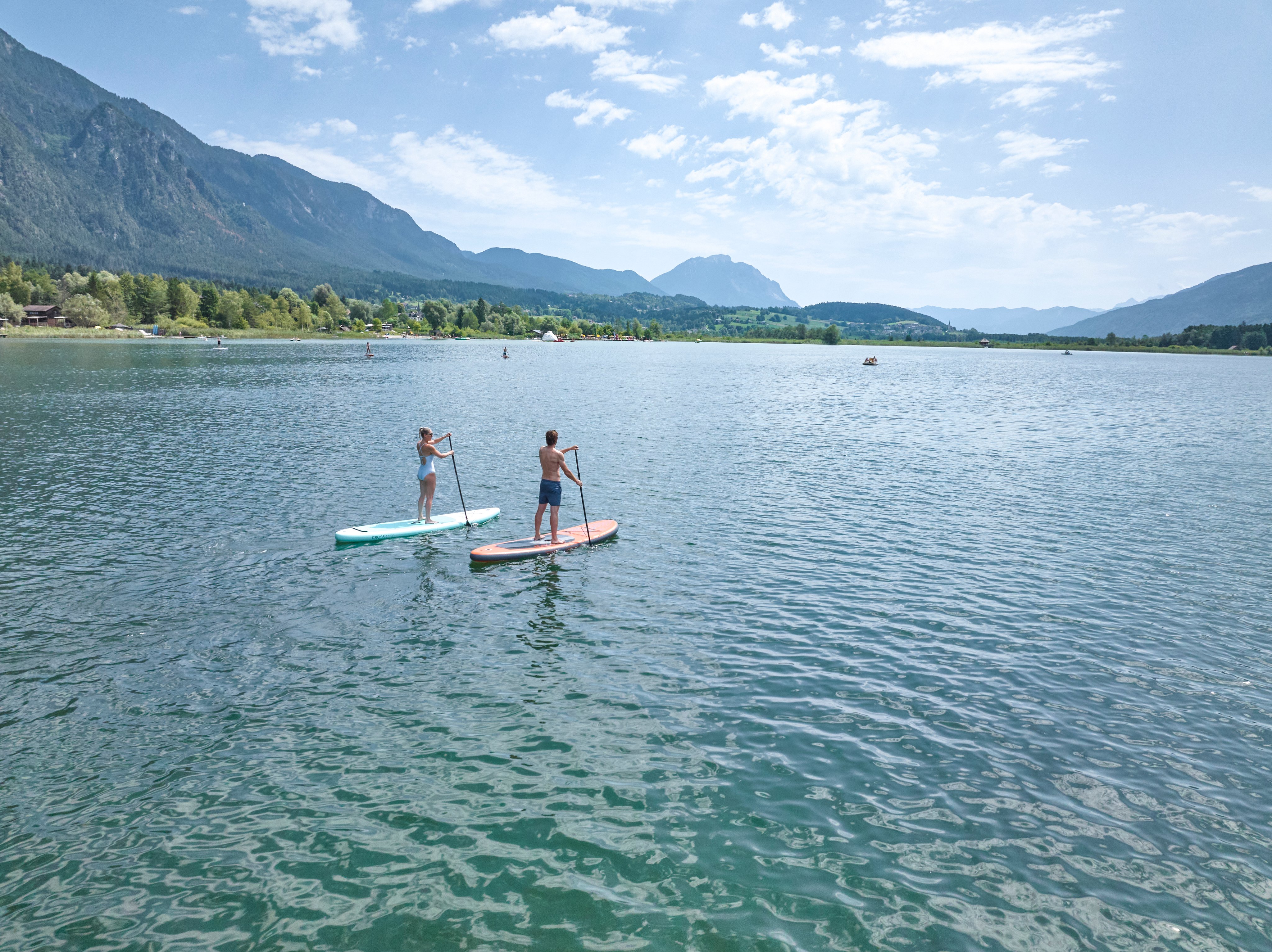 Zwei Personen beim Stand-up-Paddling auf einem ruhigen Wasser inmitten einer Berglandschaft