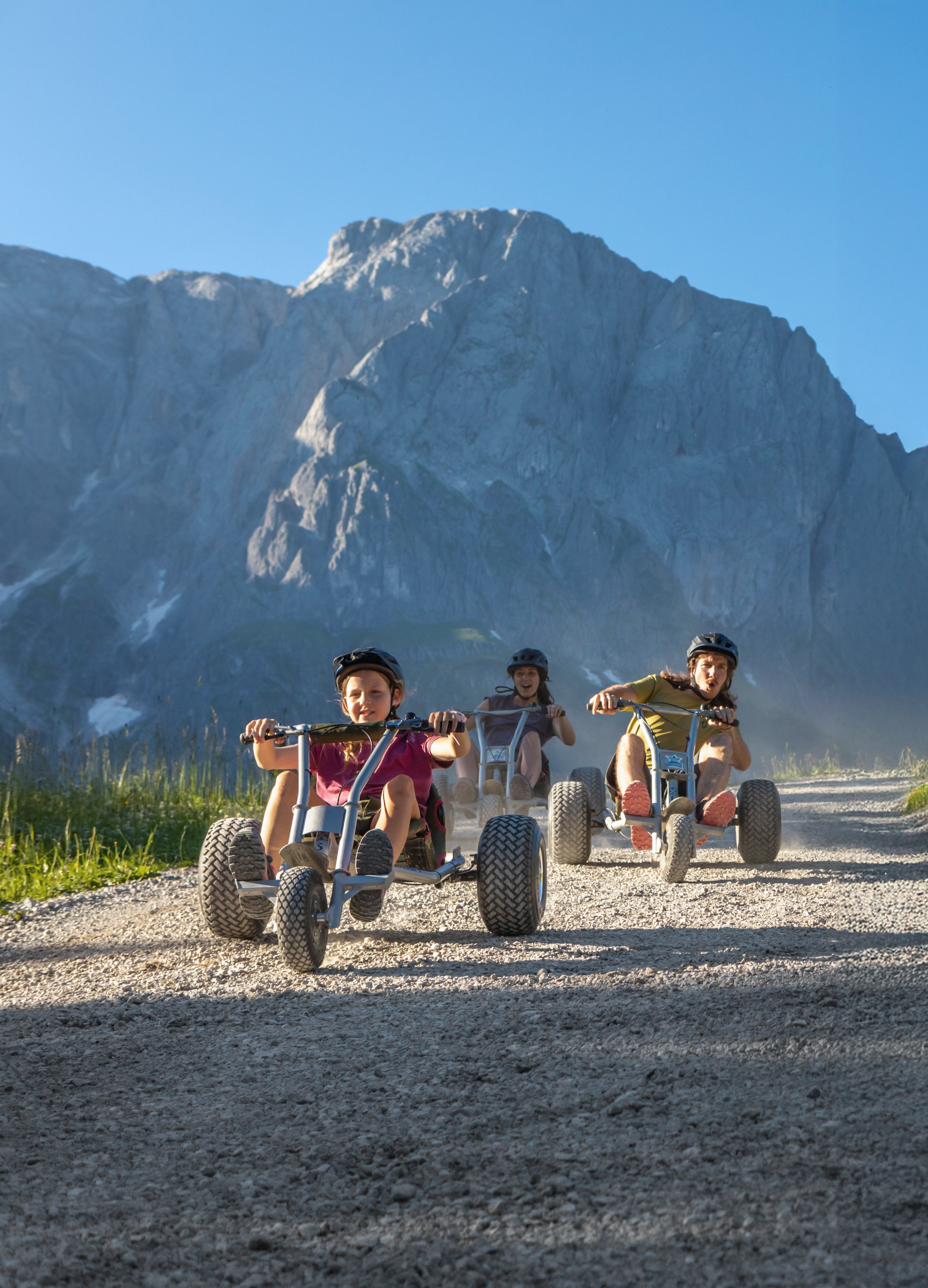 Kinder fahren mit Offroad-Gokarts im Gebirge bei Tageslicht auf Gravelweg