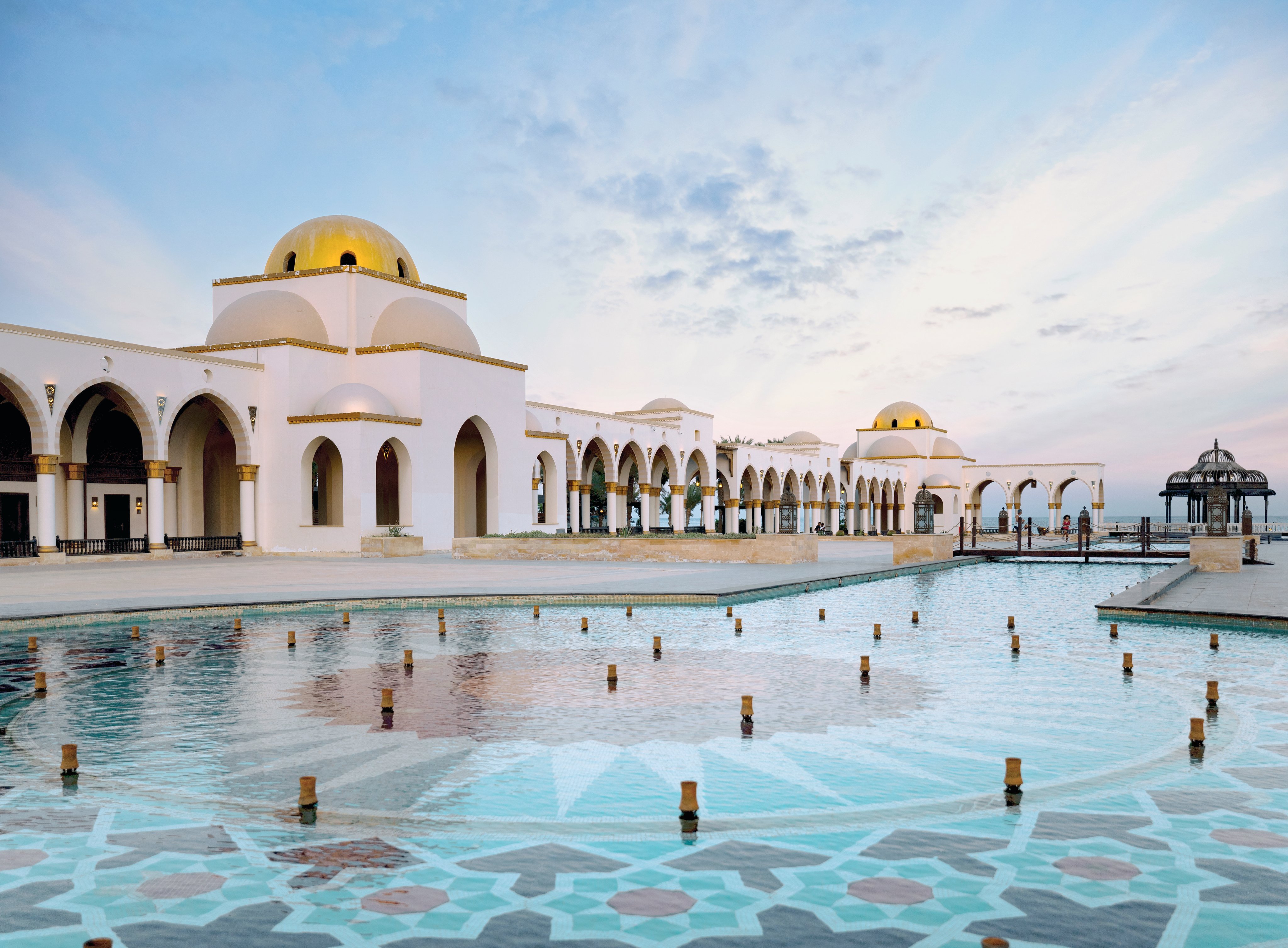 Luxuriöse weiße Hotelanlage mit goldenen Kuppeln am Wasser, ideal für Premium Cluburlaub.