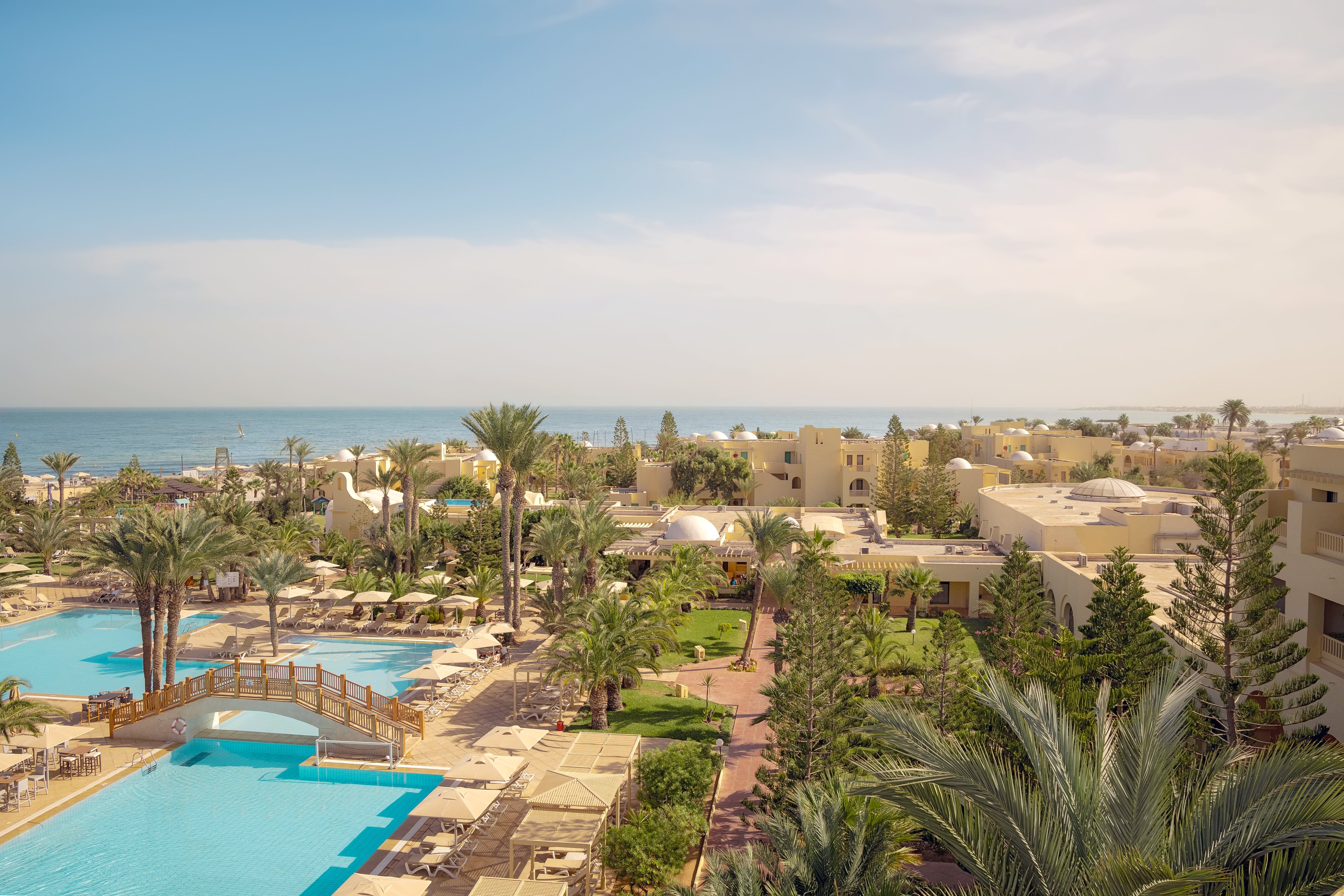 Blick auf den luxuriösen Aldiana Cluburlaub mit Pool, Palme und Meer im Hintergrund
