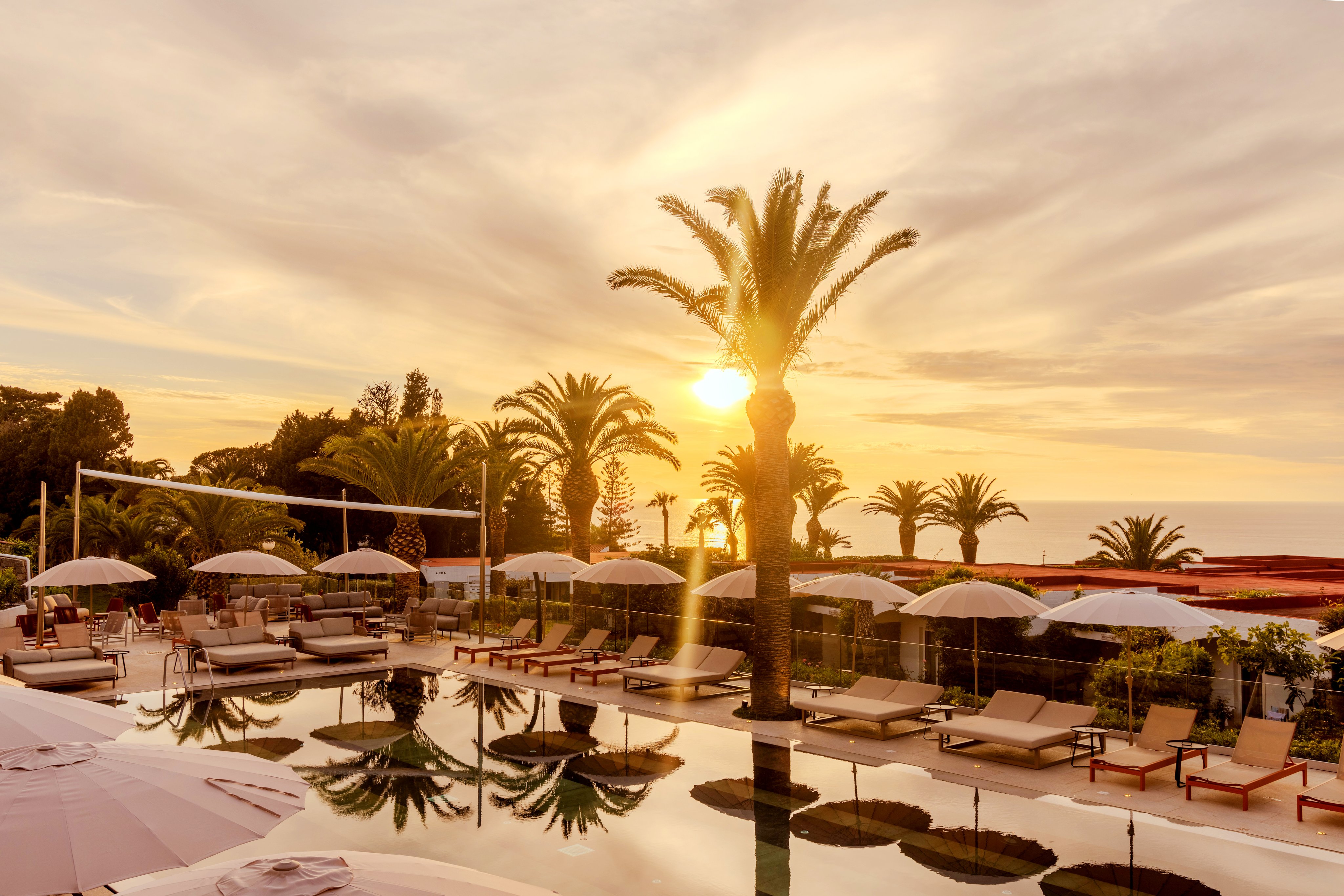 Blaue Poollandschaft mit Liegen und Palmen bei Sonnenuntergang am Aldiana Club.