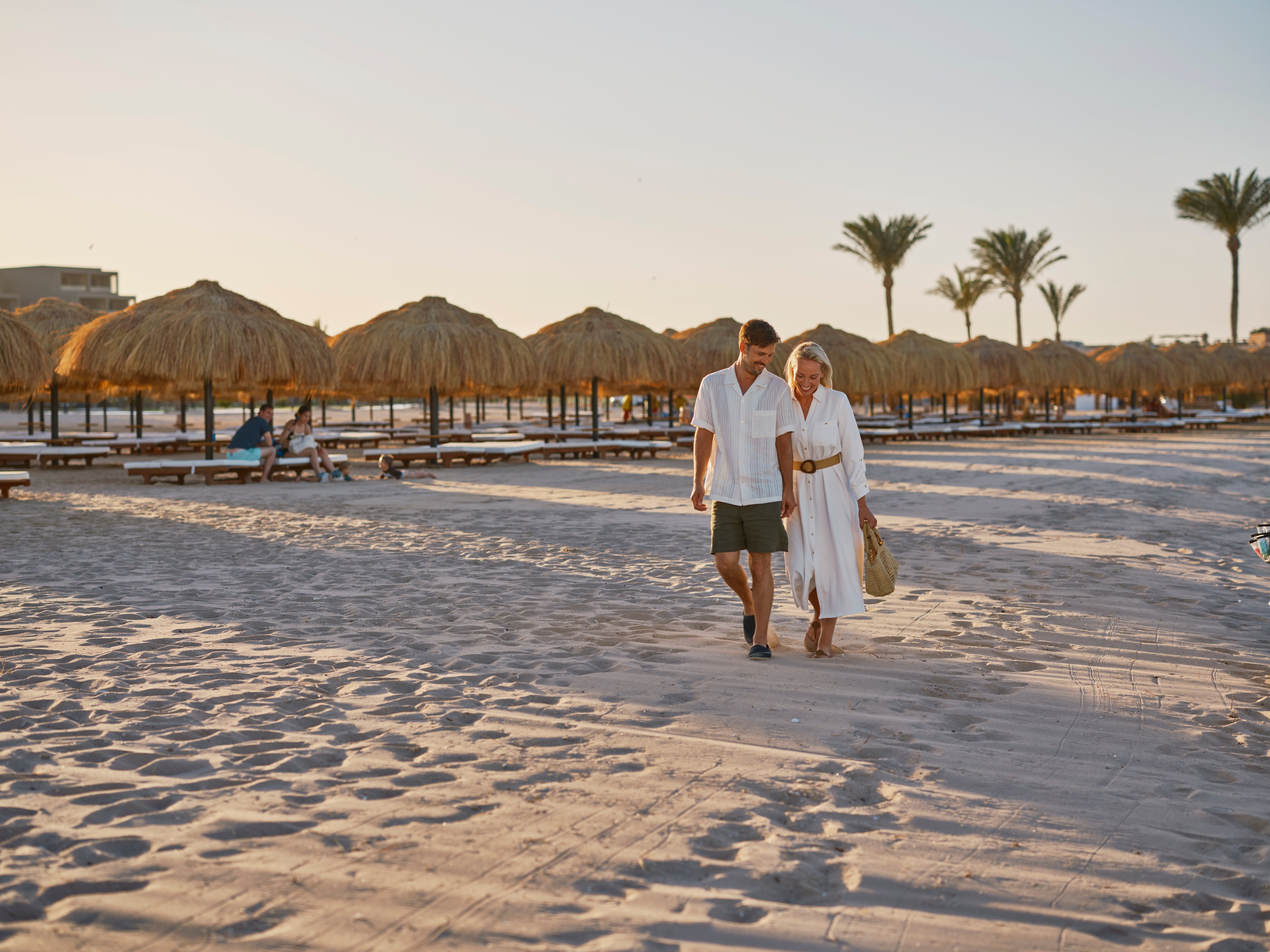 Paar spaziert am Strand mit Palmen und Sonnenschirmen bei Sonnenuntergang am Aldiana Resort