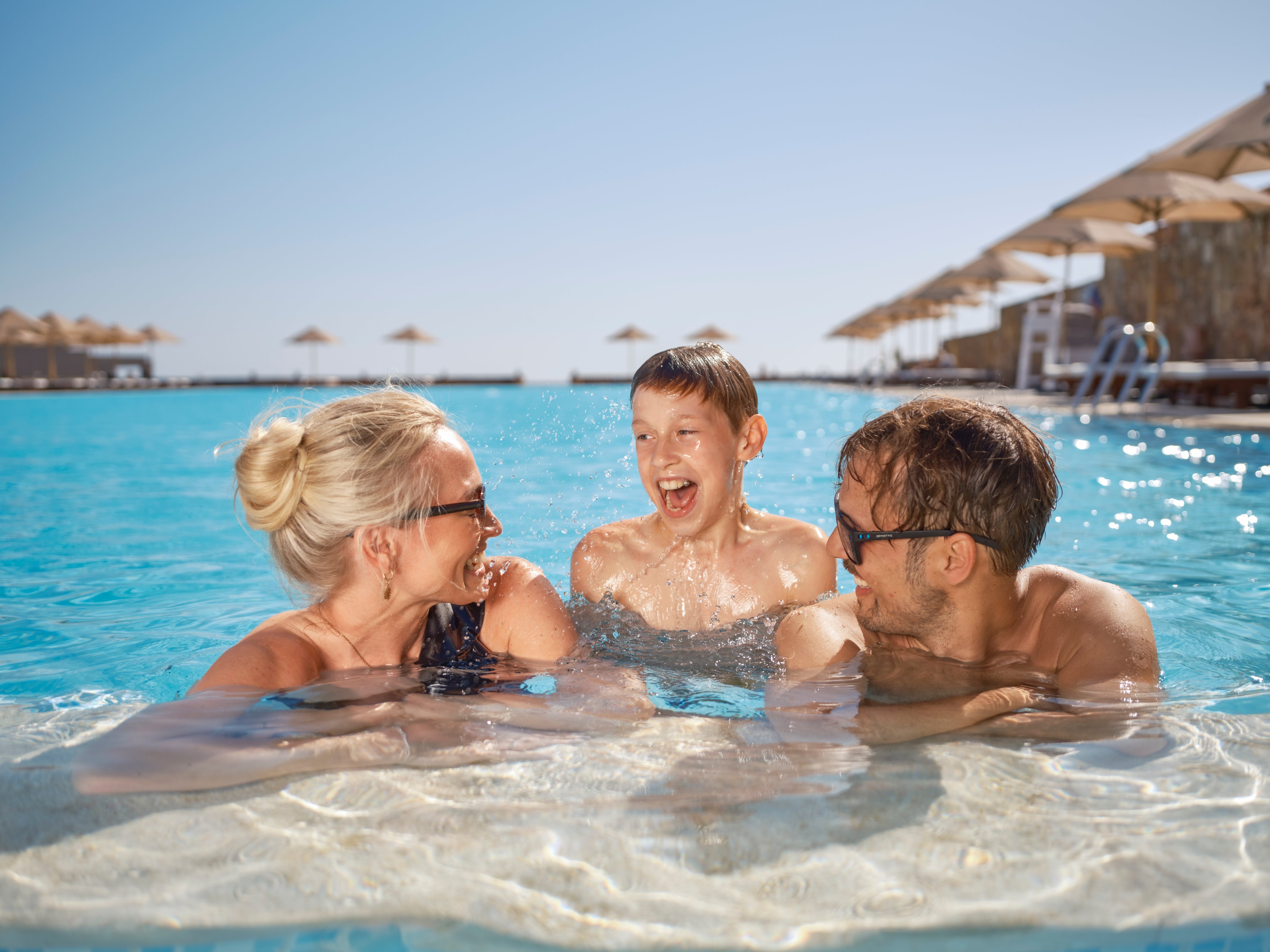 Drei Personen im Pool beim Urlaub im Aloyiana Club, sonniges Strandhotel mit Sonnenschirmen