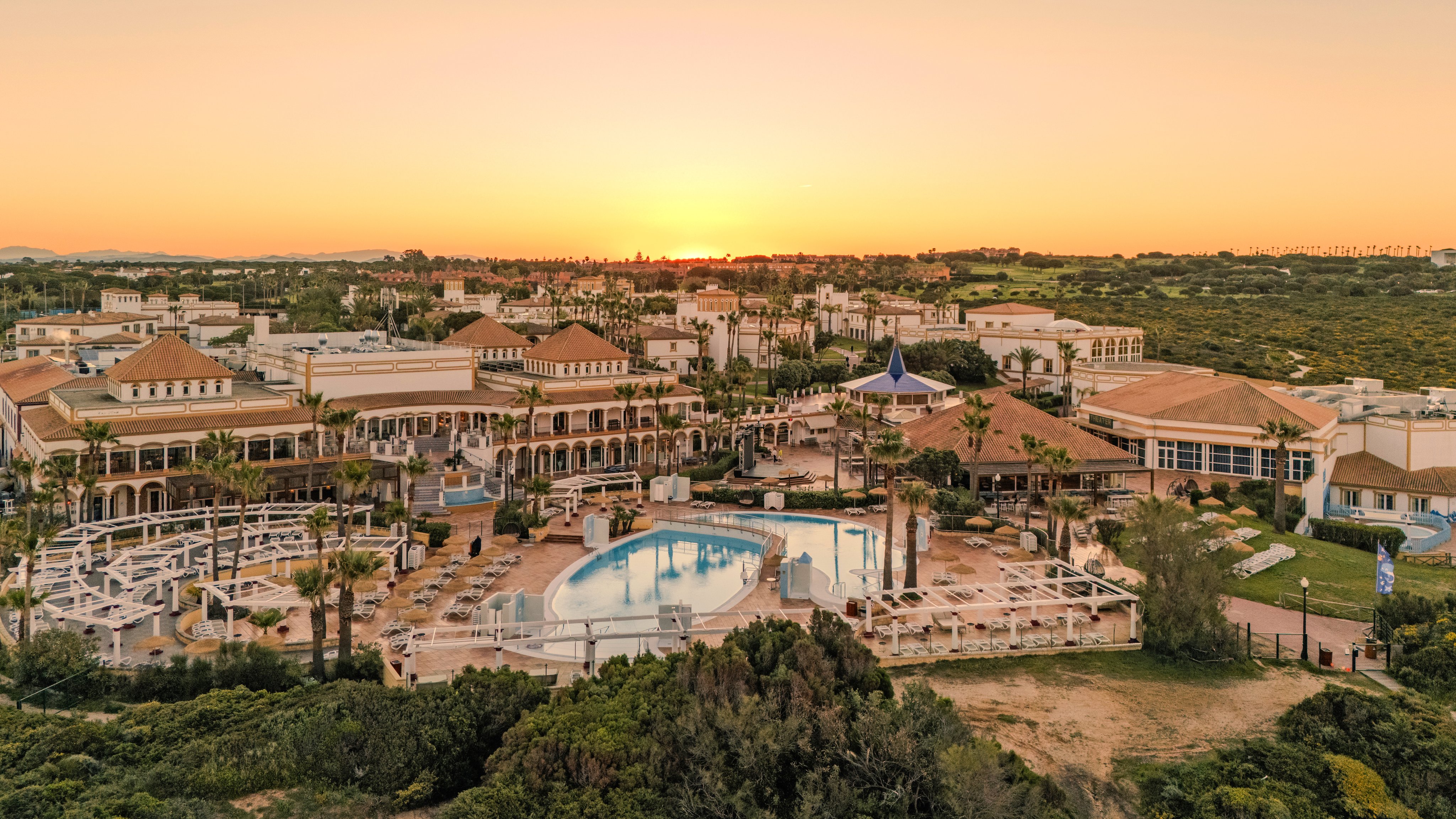 Bunter Ferienclub mit Pool, Liegen und gepflegter Anlage bei Sonnenuntergang