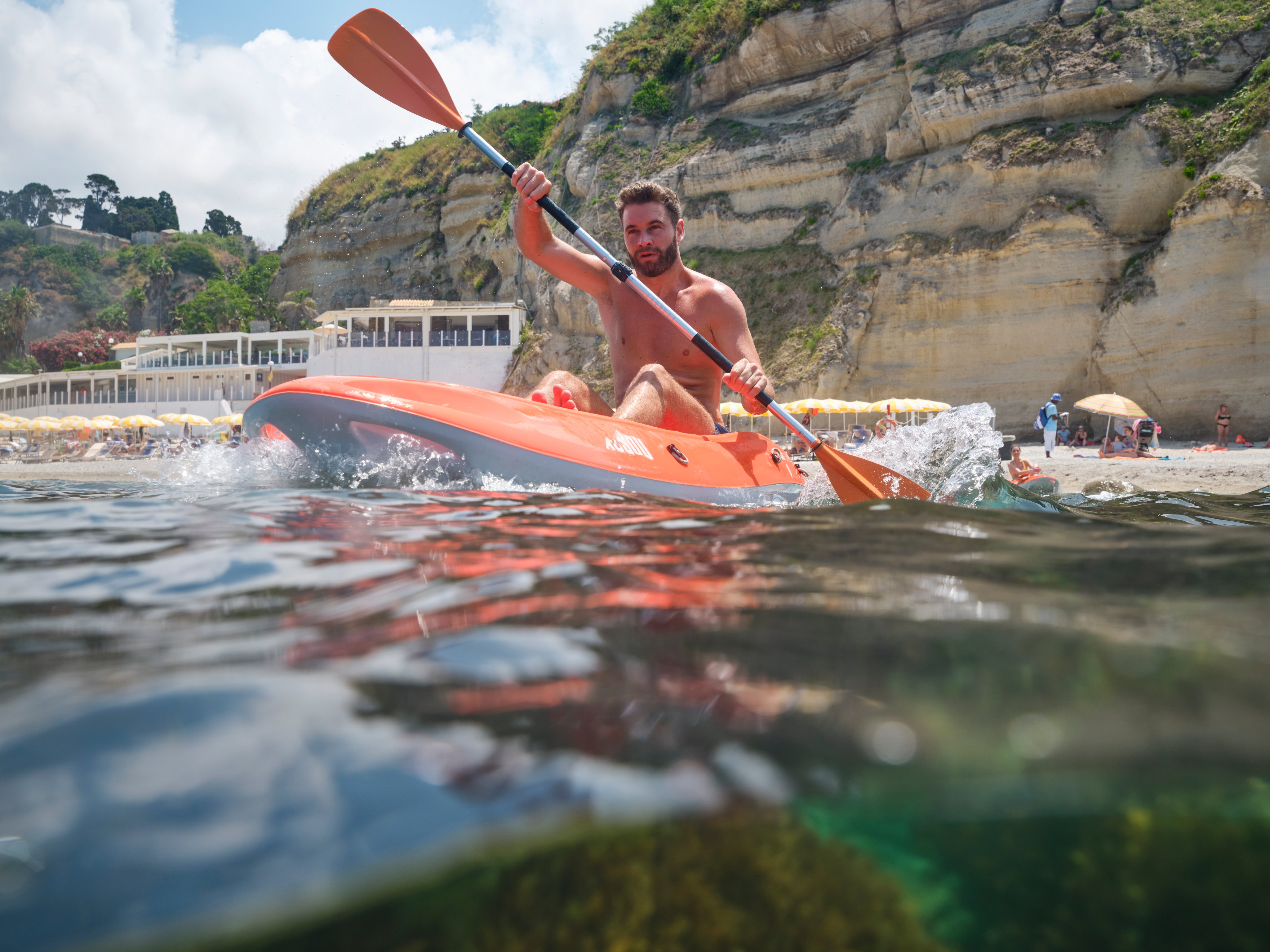 Person beim Kayakfahren an einem Strand mit Felsen im Hintergrund