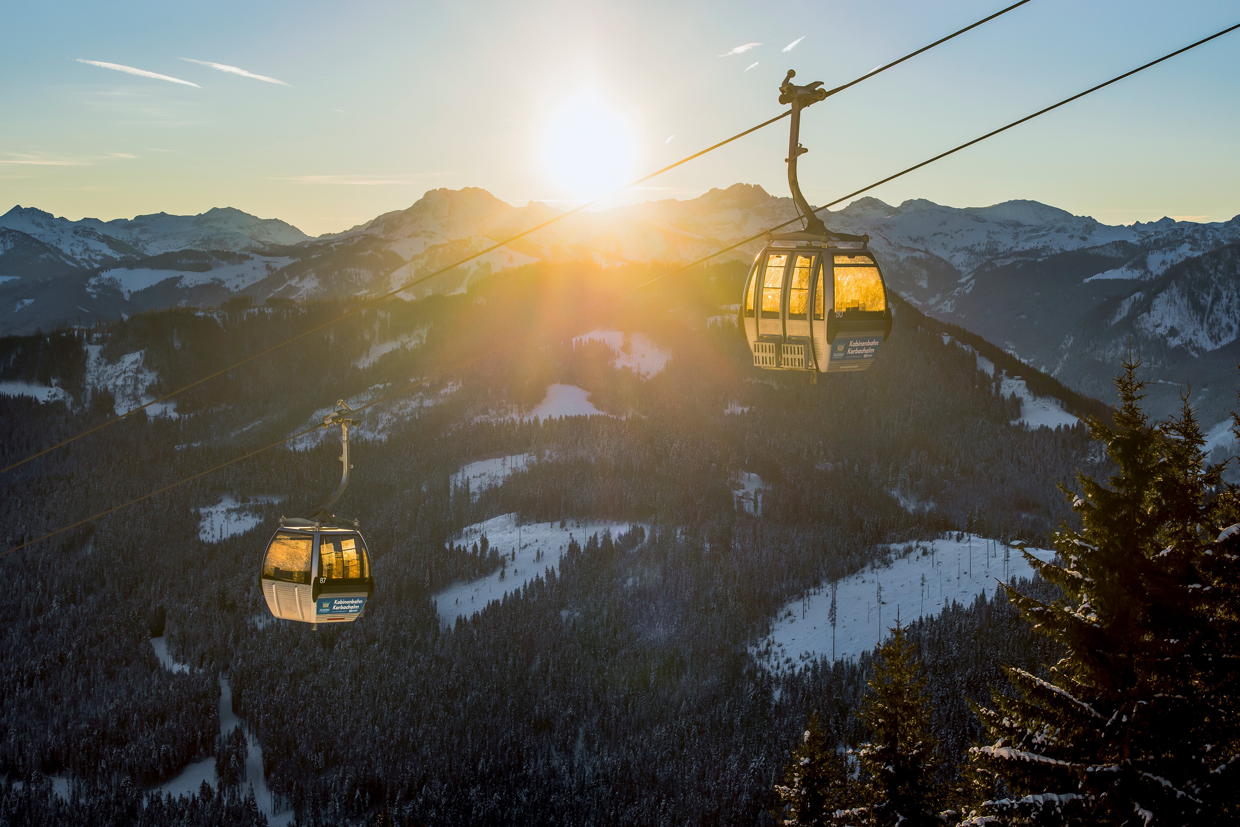 Zwei Gondeln in den Bergen bei Sonnenuntergang, Blick auf verschneite Berge und Wälder